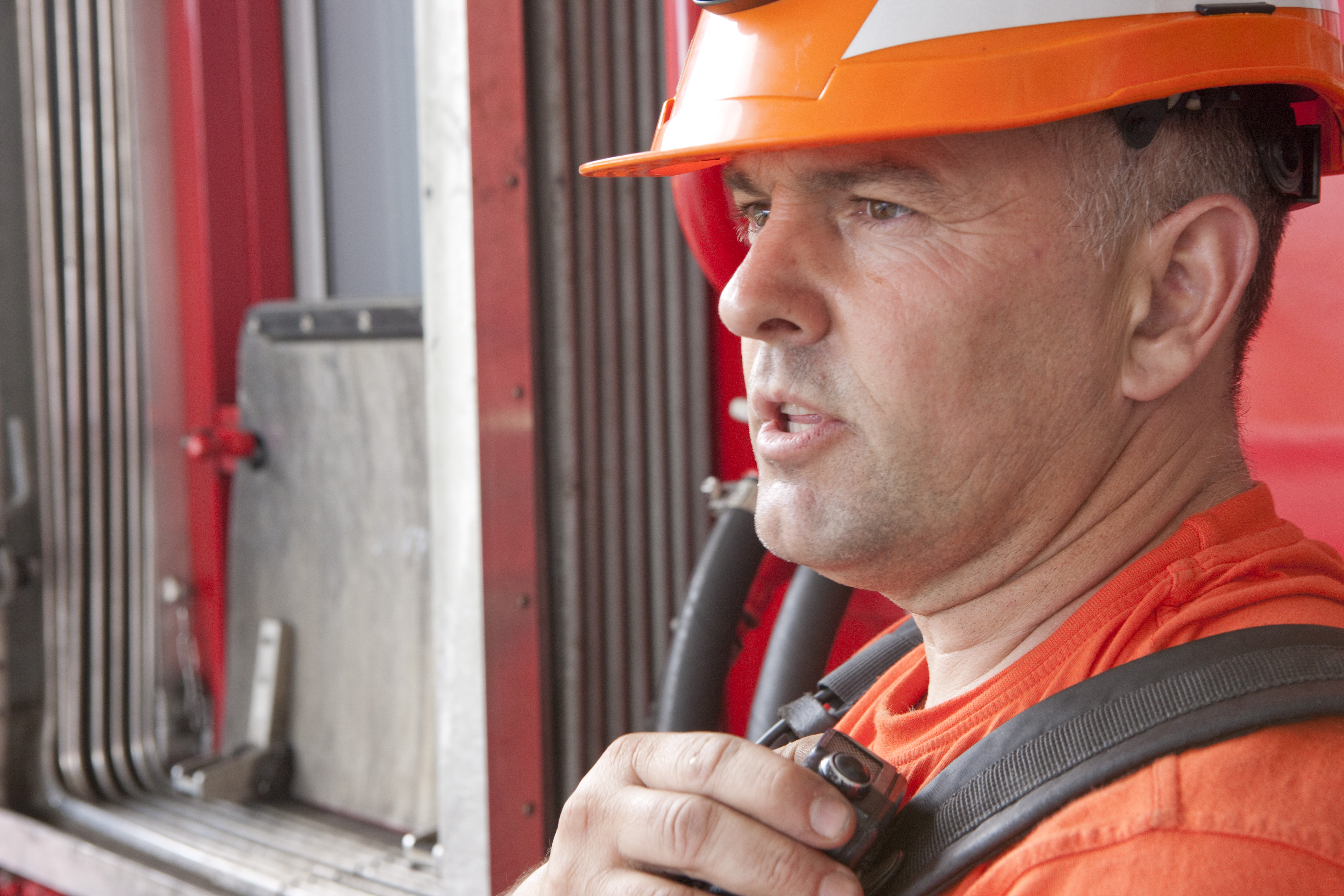 Ein Mitarbeiter der Rhätischen Bahn mit oranger Schutzkleidung und Helm spricht in ein Funkgerät.