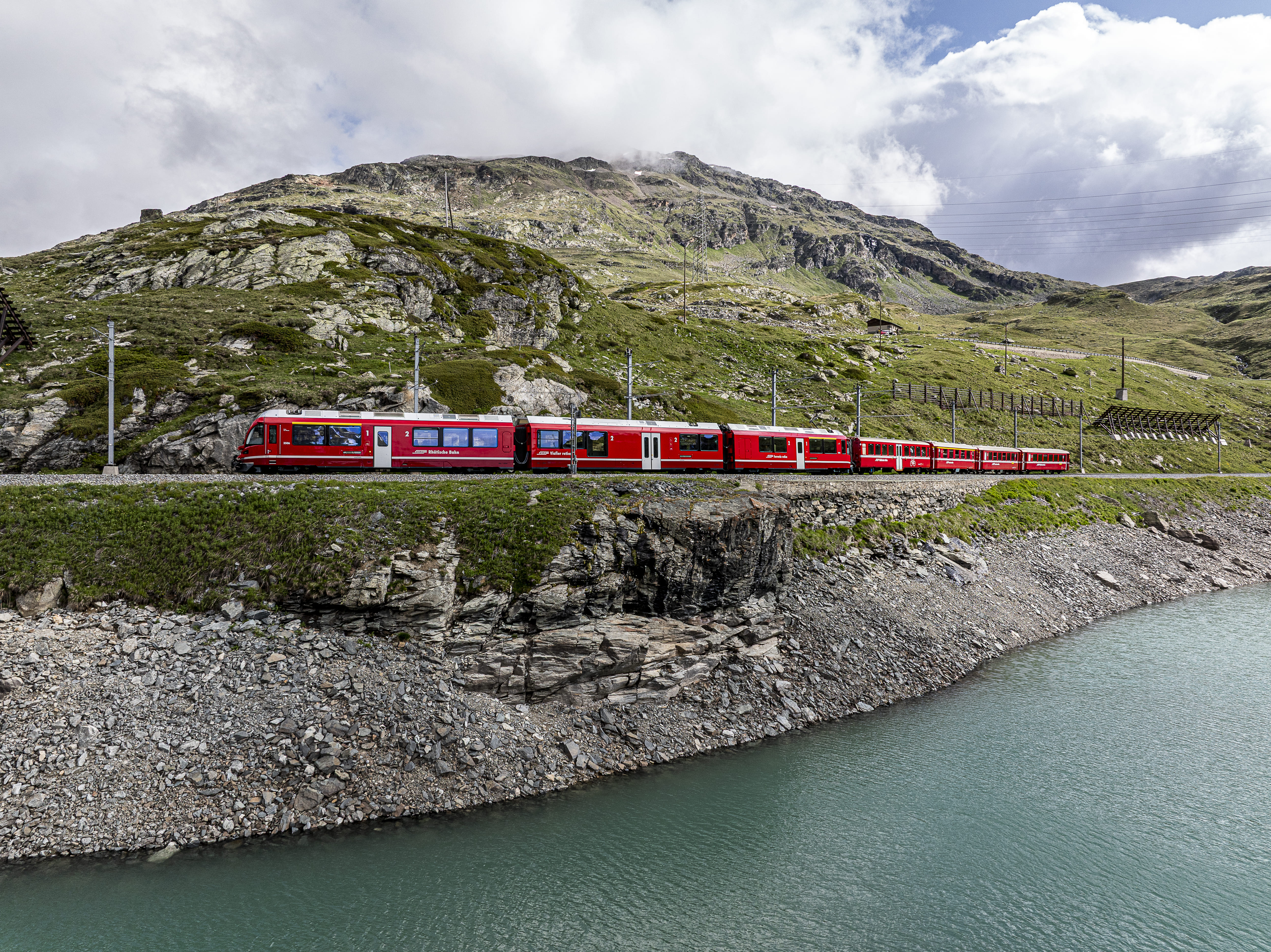 Regionalzug der Rhätischen Bahn fährt am Lago Bianco vorbei, eingebettet in eine beeindruckende Berglandschaft.