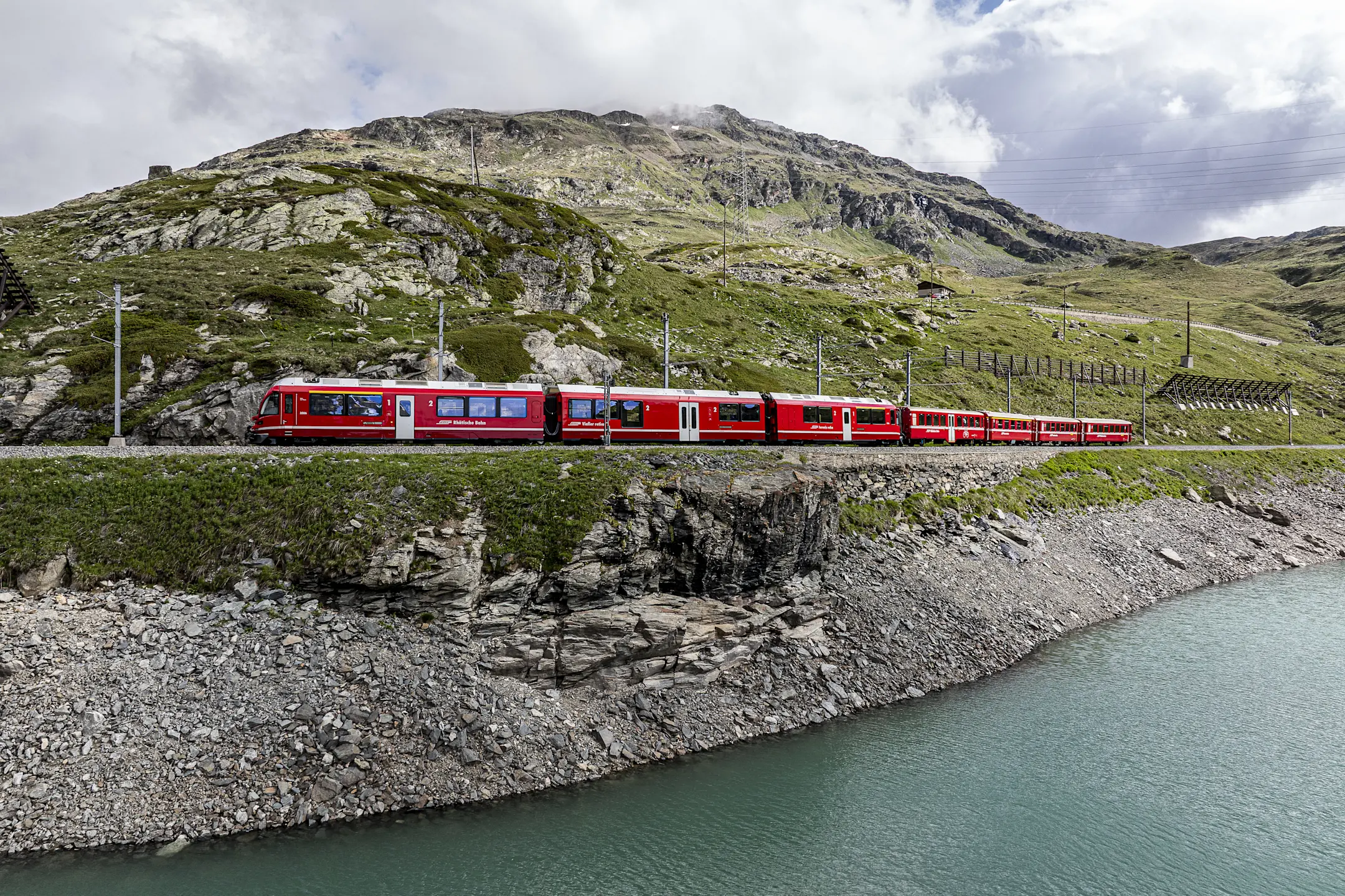 Regionalzug der Rhätischen Bahn fährt am Lago Bianco vorbei, eingebettet in eine beeindruckende Berglandschaft.