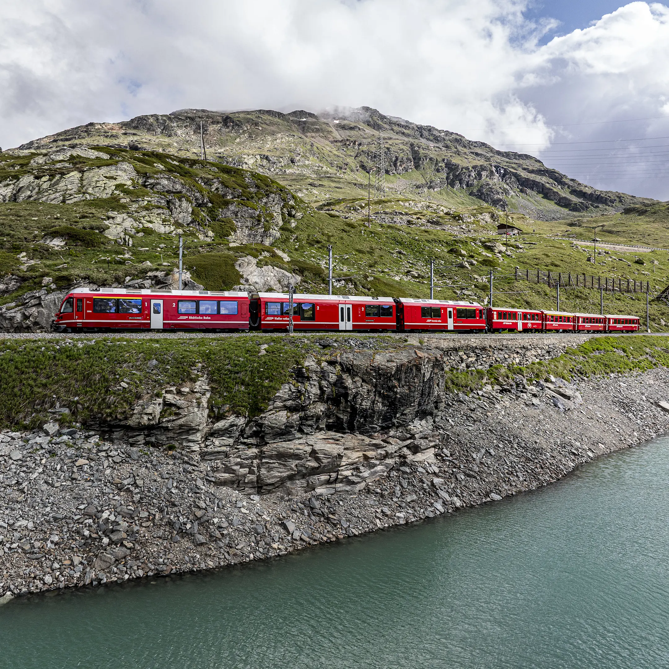 Regionalzug der Rhätischen Bahn fährt am Lago Bianco vorbei, eingebettet in eine beeindruckende Berglandschaft.