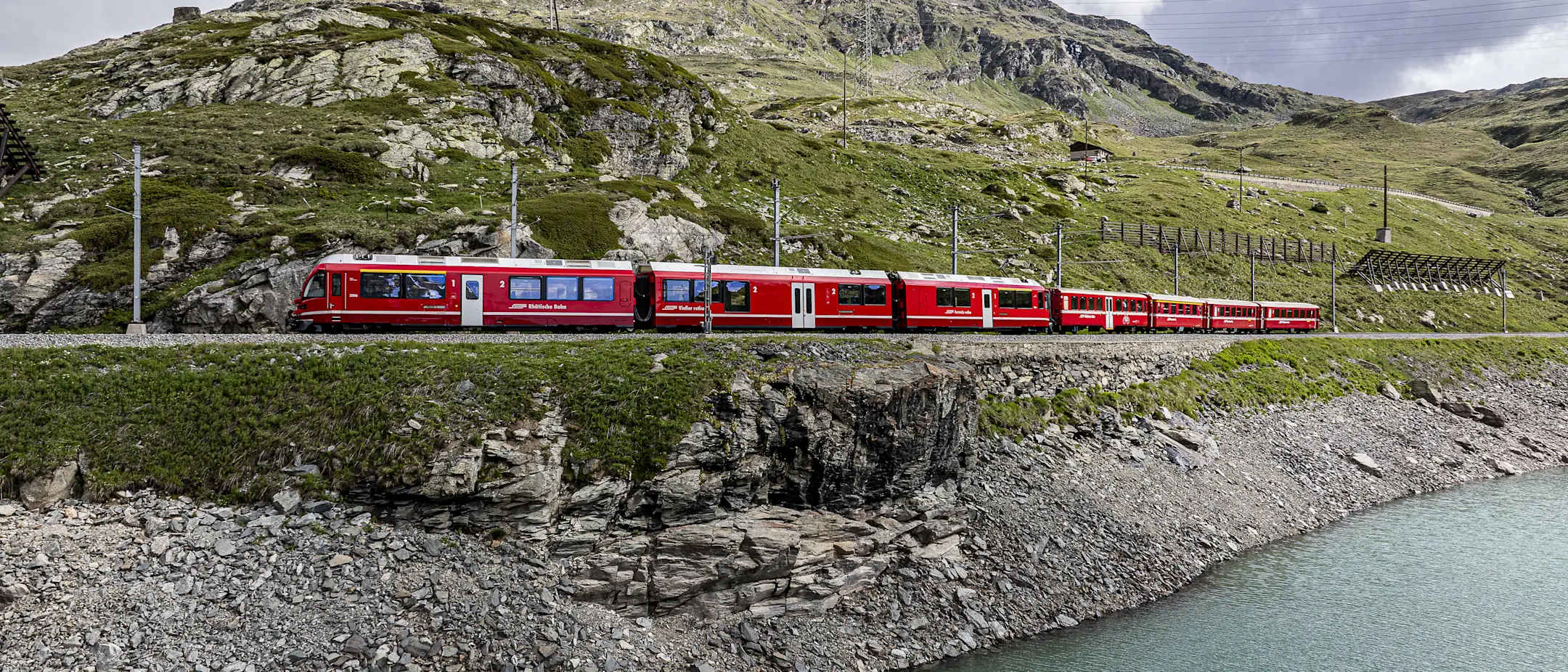 Regionalzug der Rhätischen Bahn fährt am Lago Bianco vorbei, eingebettet in eine beeindruckende Berglandschaft.