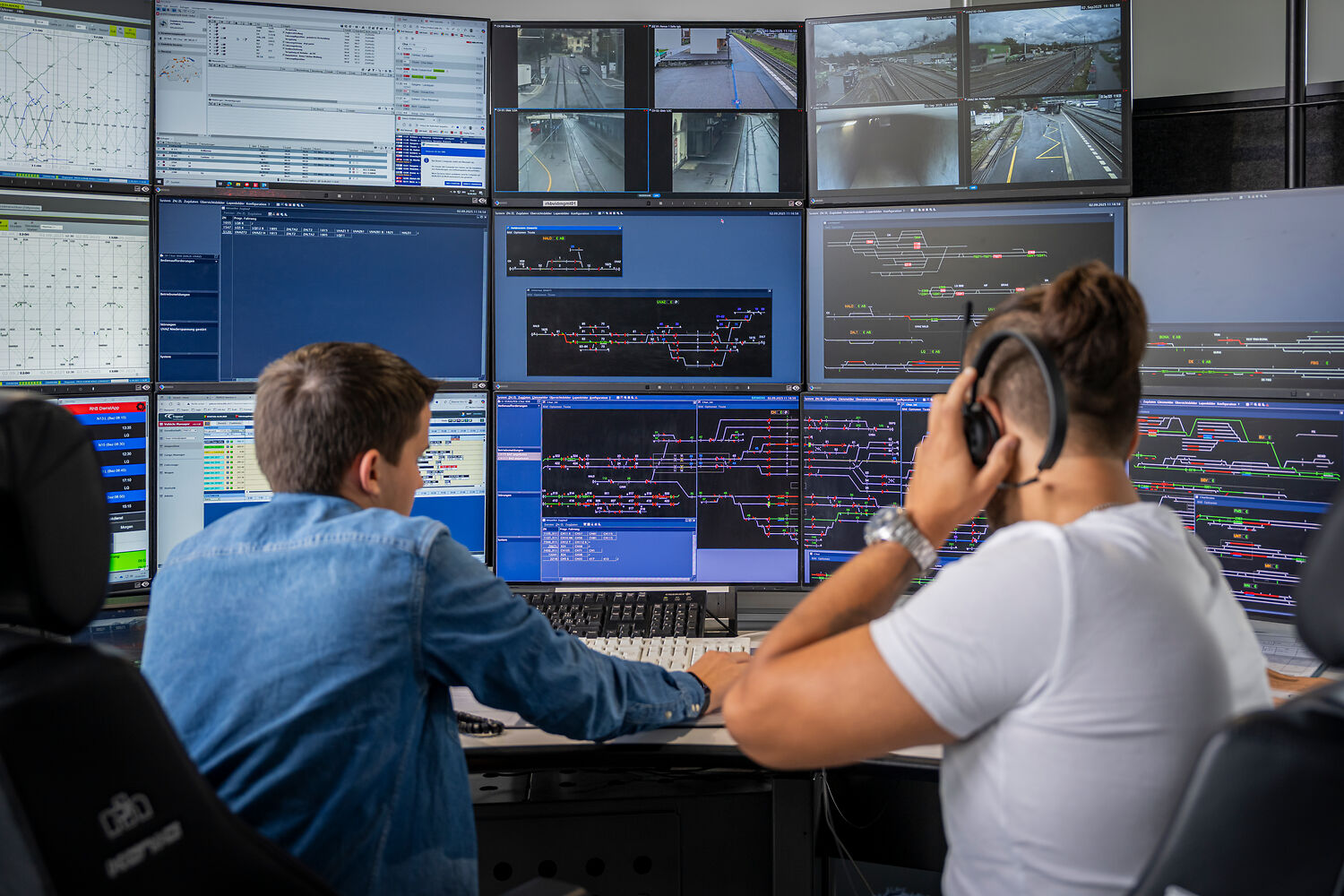 Train dispatcher at work, with a trainee on the left, surrounded by numerous screens