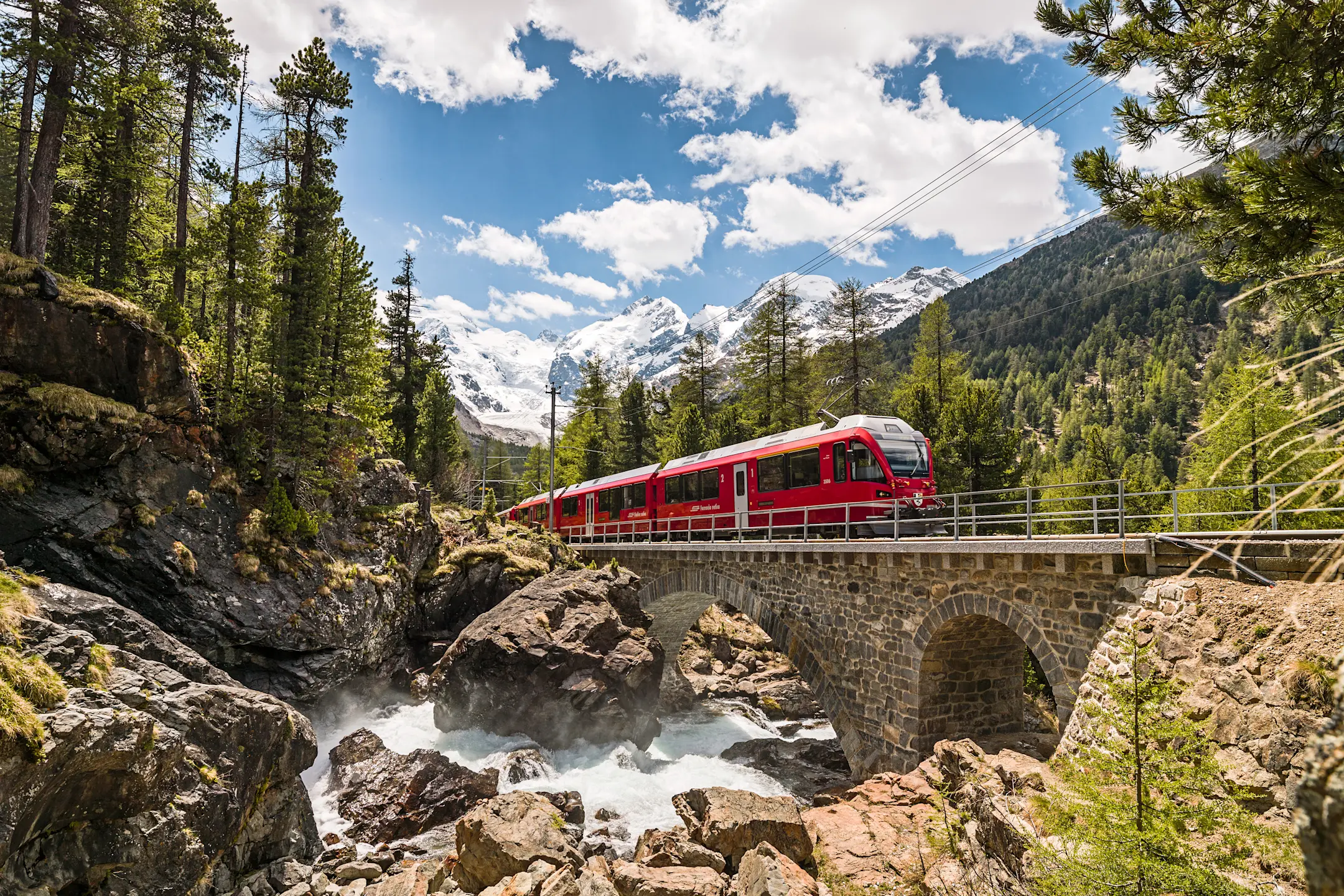 Ein Regionalzug der RhB überquert bei Morteratsch den Berninabach. Im Hintergrund ist der Morteratschgletscher sichtbar.