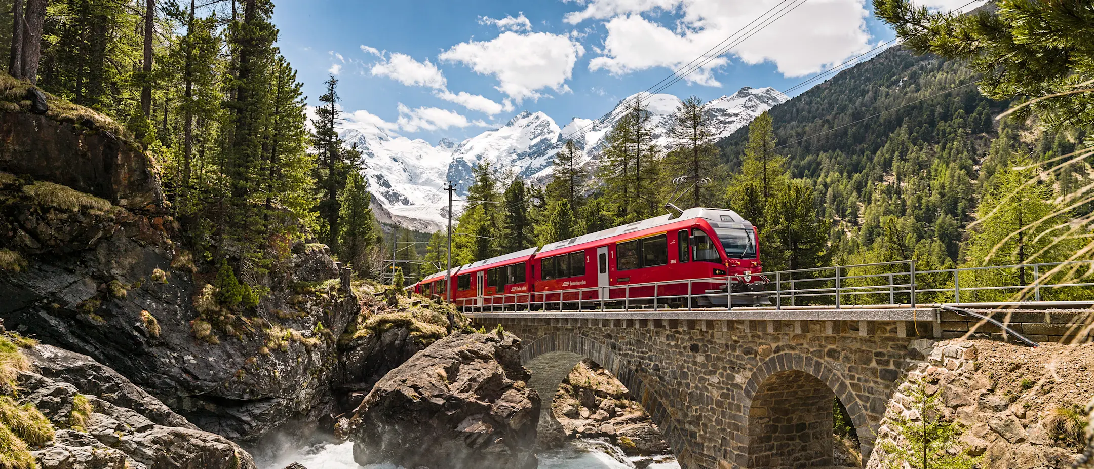 Ein Regionalzug der RhB überquert bei Morteratsch den Berninabach. Im Hintergrund ist der Morteratschgletscher sichtbar.