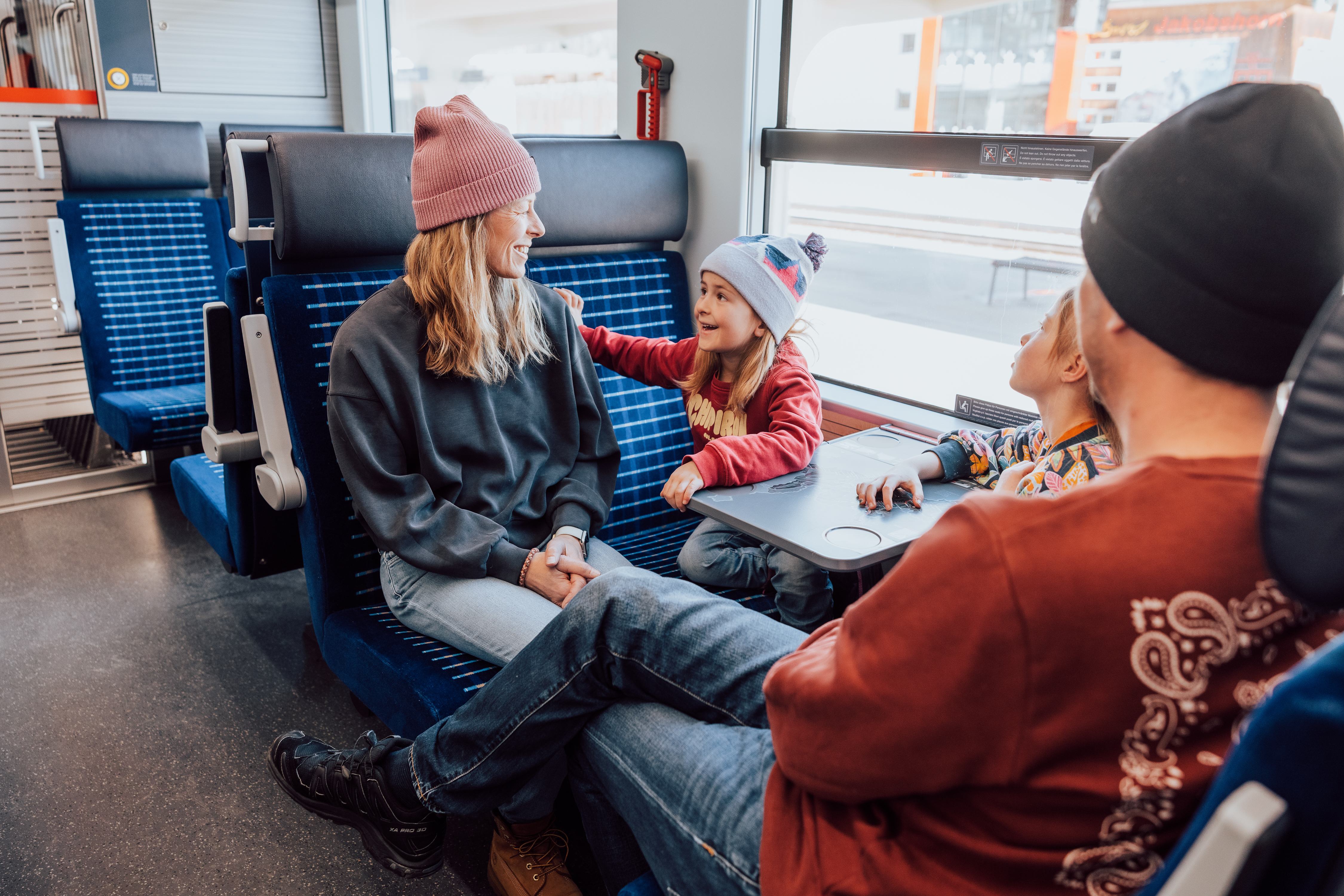 Eine Familie mit zwei Kindern sitzt in einem modernen RhB-Zug und geniesst die entspannte Fahrt im komfortablen Abteil.