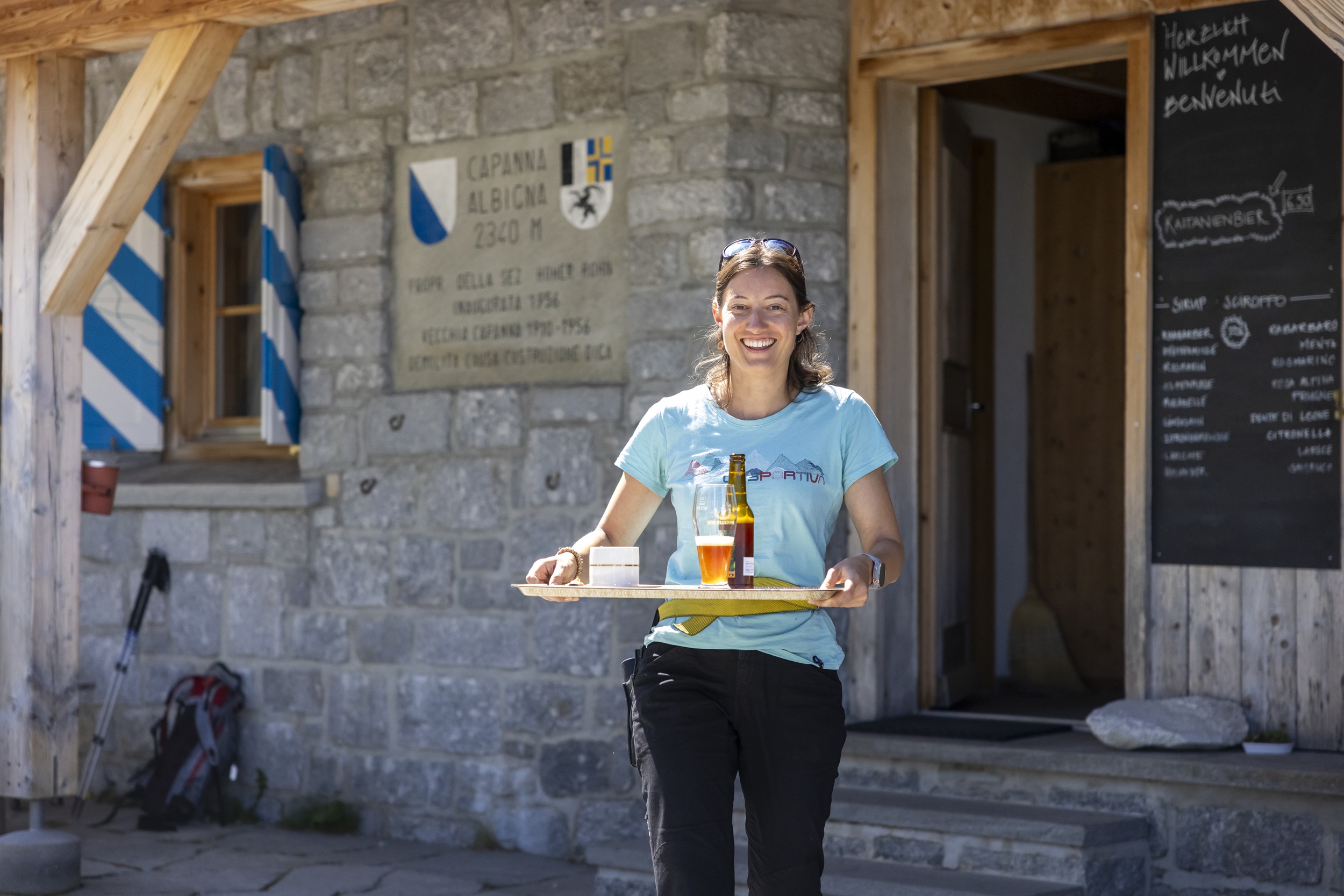 Eine Frau läuft mit einem Tablett voller Getränke aus der Berghütte.