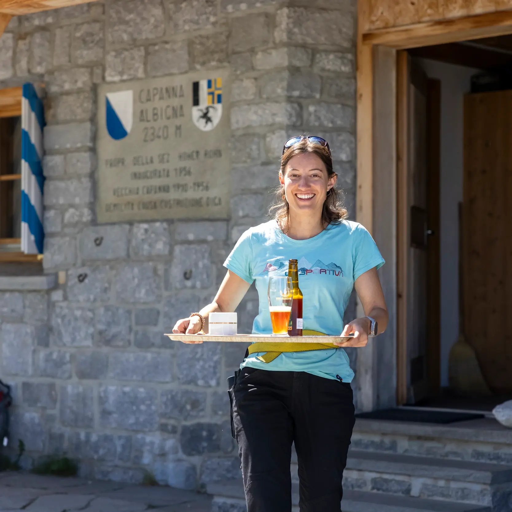 Eine Frau läuft mit einem Tablett voller Getränke aus der Berghütte.