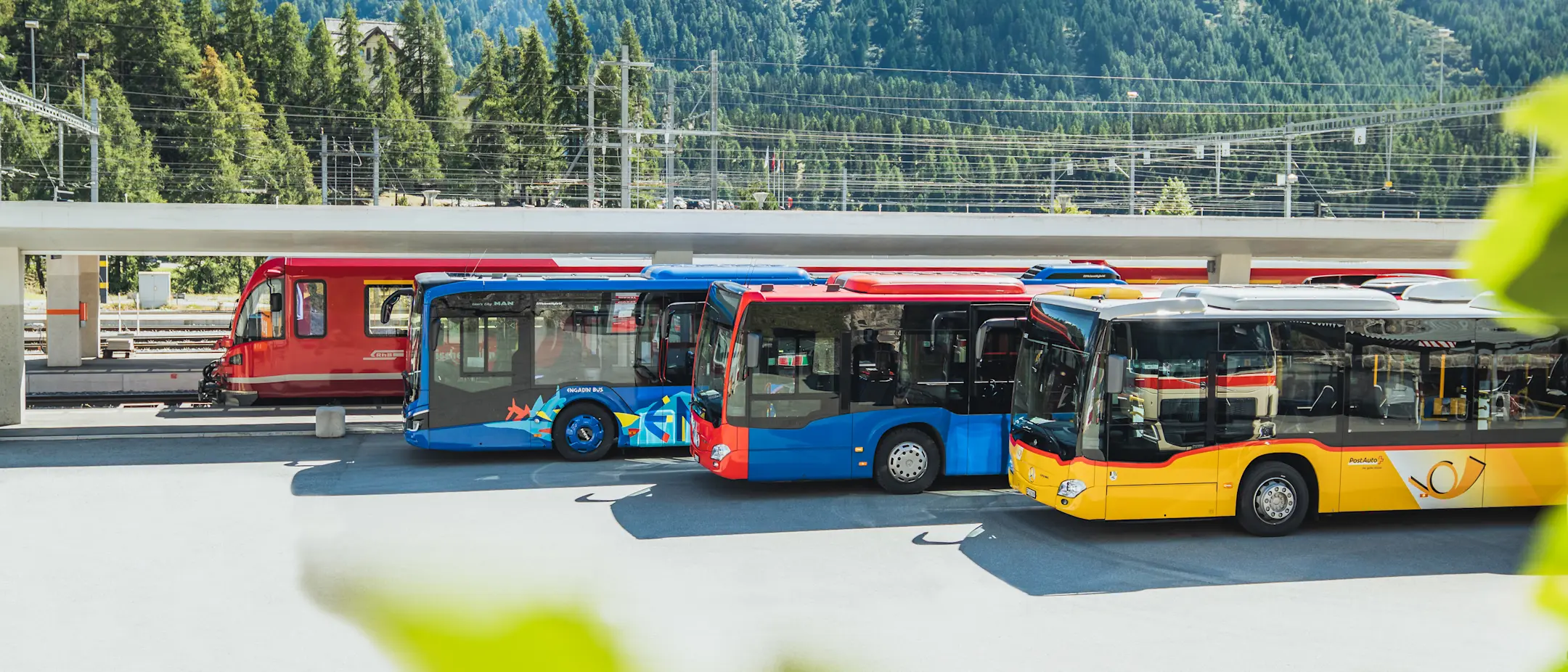 Ein RhB-Zug, zwei Busse von Engadin Bus und ein Postauto am Bahnhof Pontresina.