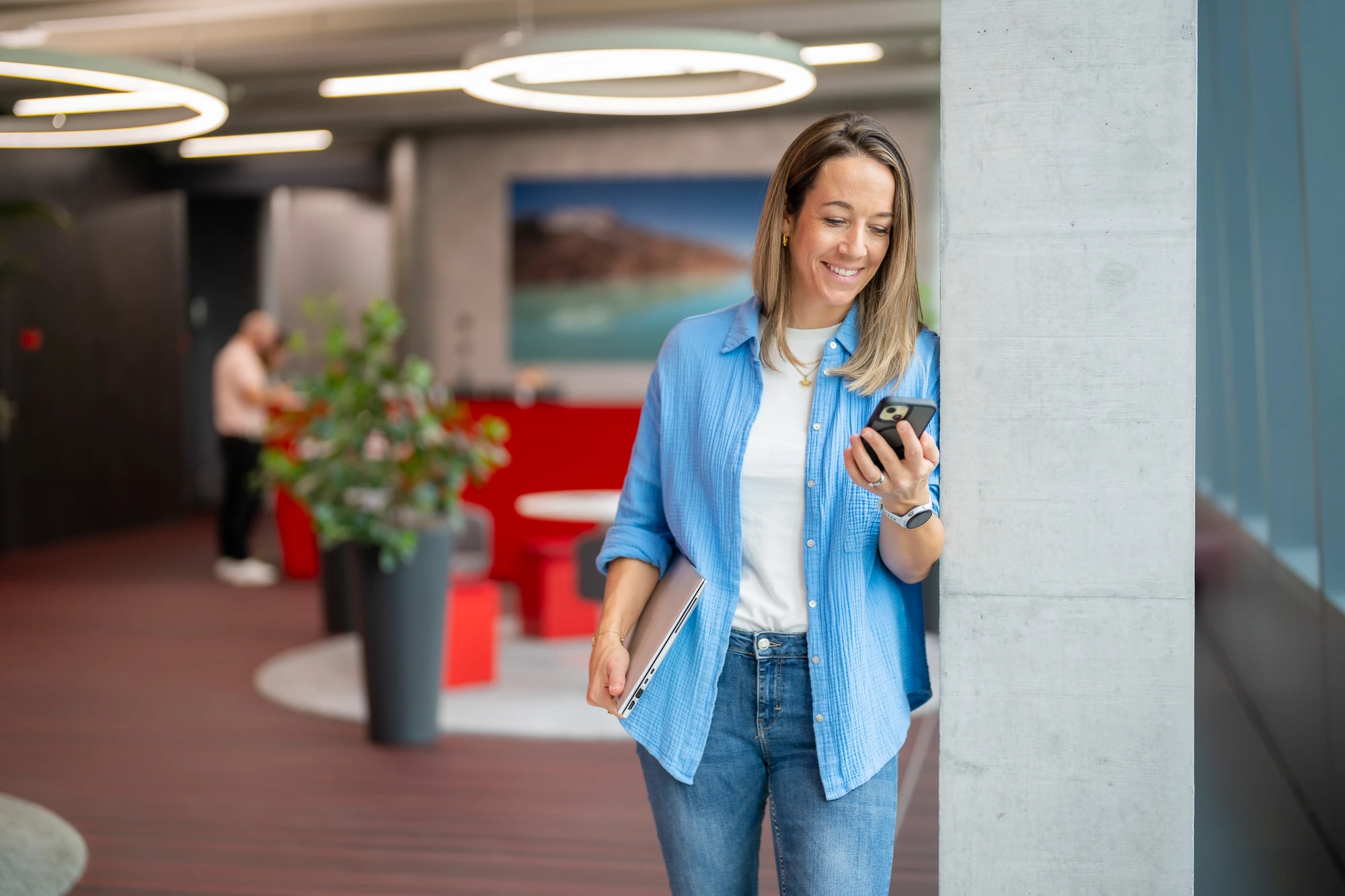 Eine Mitarbeiterin steht mit Handy im Bürogebäude Rollmaterial und lacht