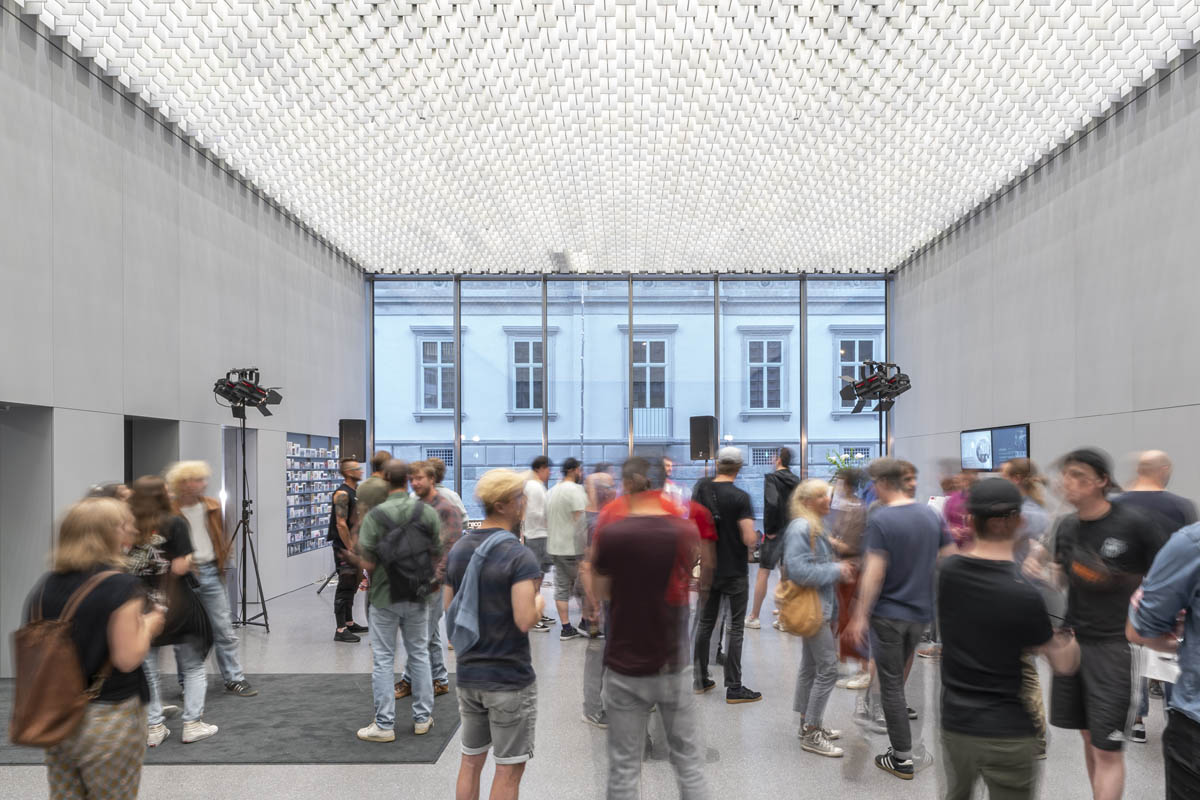 Menschen schlendern durch den modernen Eingangsbereich des Bündner Kunstmuseums mit hoher Lichtdecke und großen Glasfenstern.