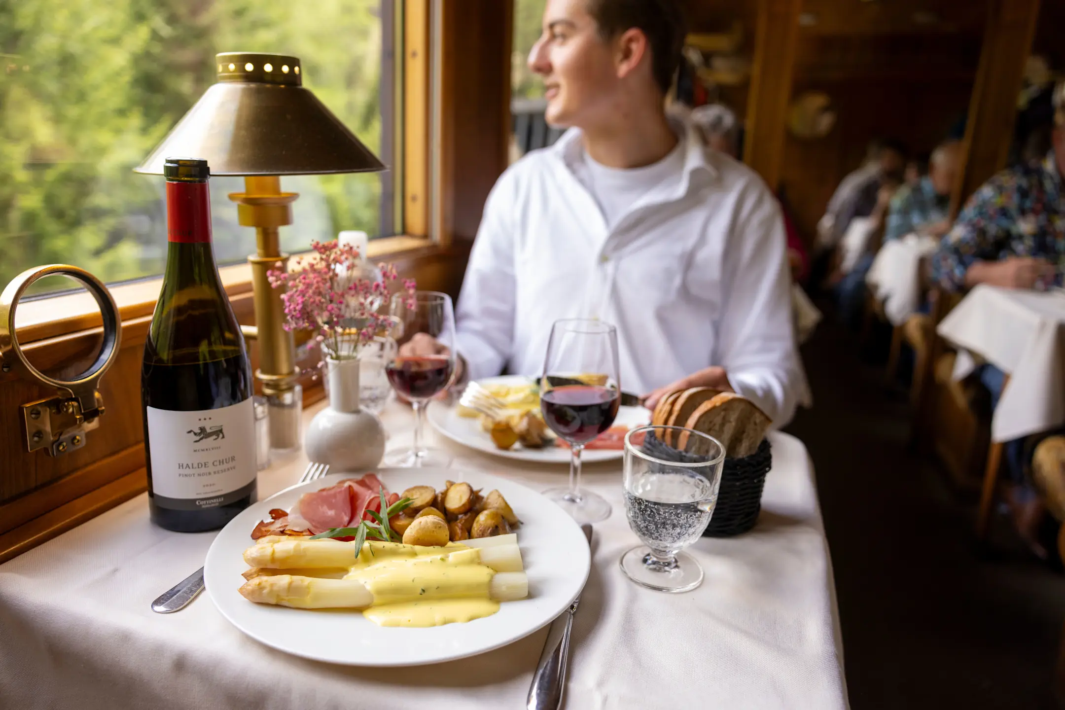 Ein Gast sitzt am weiss gedeckten Tisch im Gourmino, vor ihm liegt ein Teller mit weissen Spargeln, Schinken und Kartoffeln.
