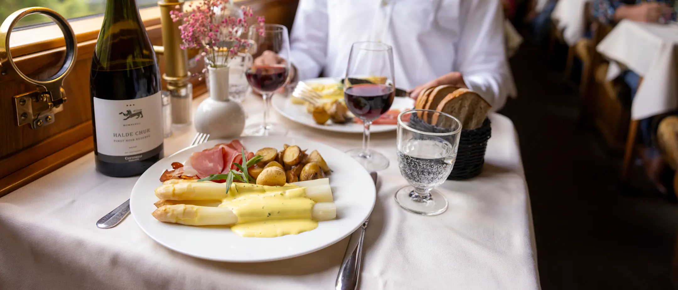 Ein Gast sitzt am weiss gedeckten Tisch im Gourmino, vor ihm liegt ein Teller mit weissen Spargeln, Schinken und Kartoffeln.
