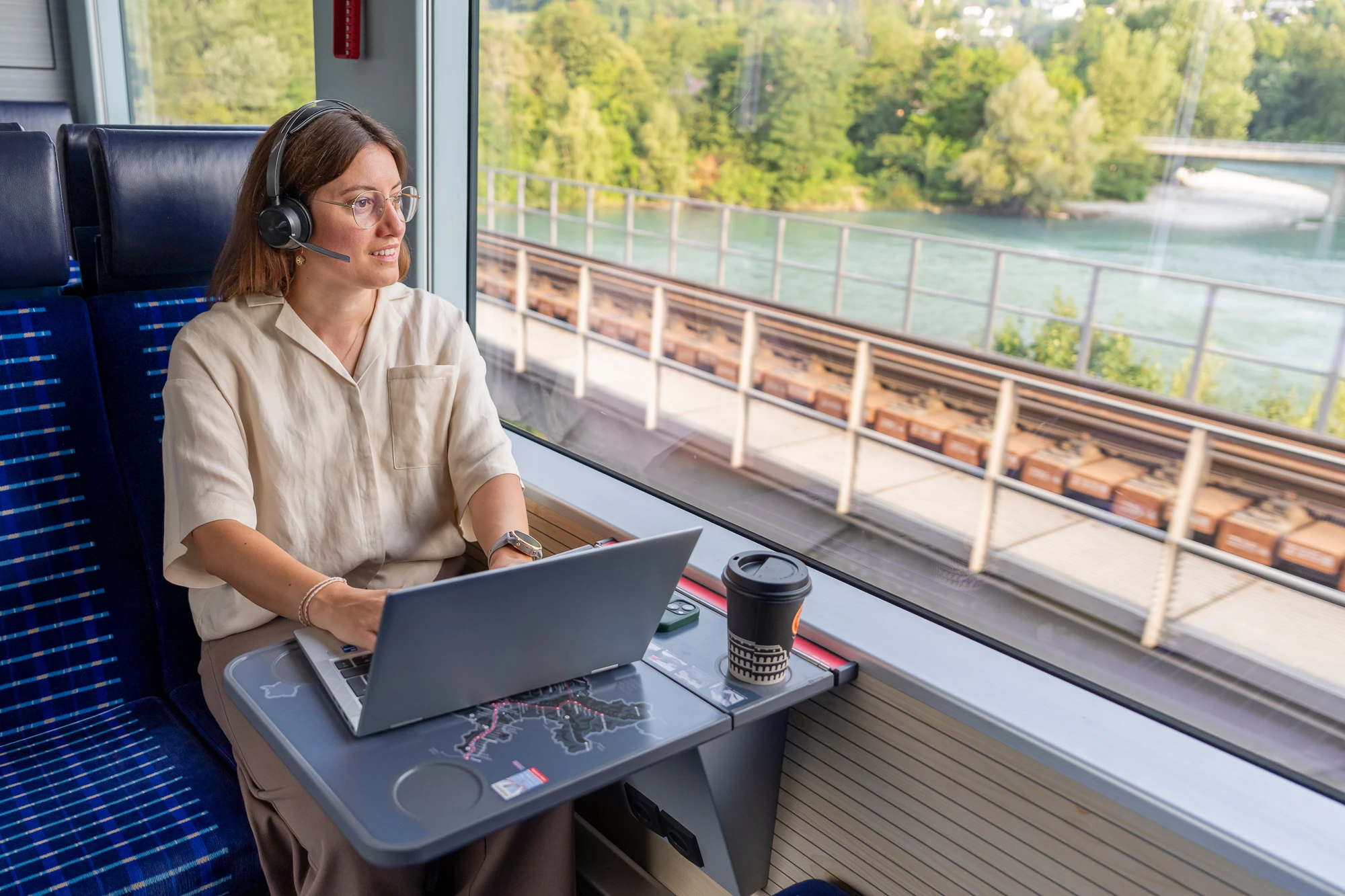 Mitarbeiterin arbeitet im Zug am Laptop und schaut aus dem Fenster