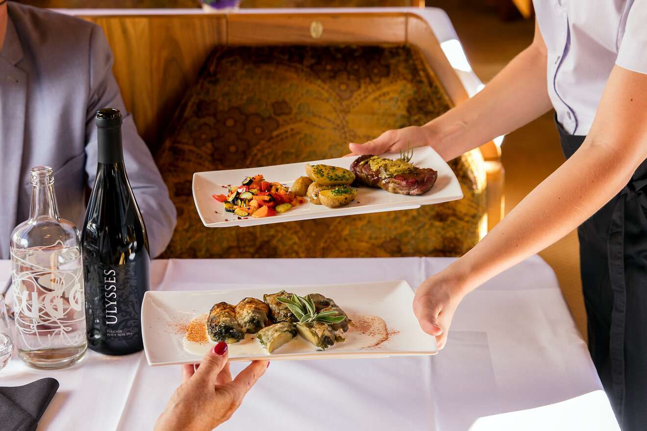 Un addetto al servizio serve due portate principali elegantemente impiattate a bordo della carrozza ristorante «Gourmino».
