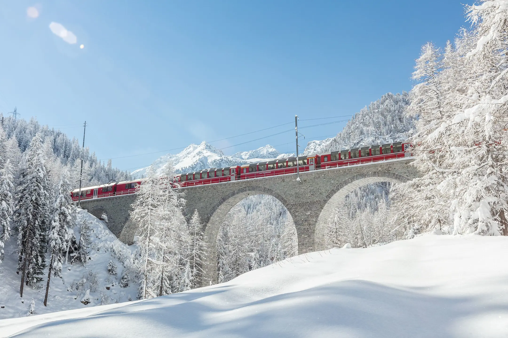 Der Bernina Express fährt in der Winterlandschaft über den Albulaviadukt.