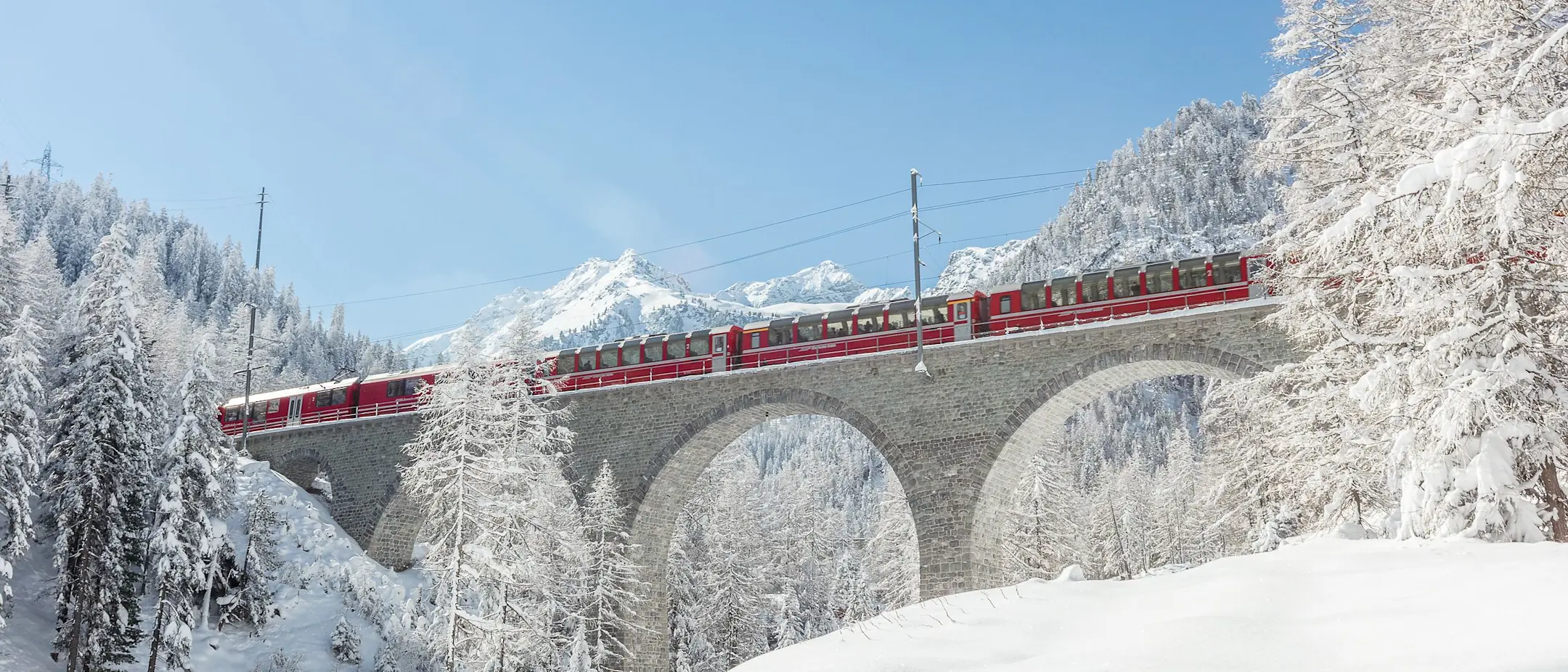Der Bernina Express fährt in der Winterlandschaft über den Albulaviadukt.