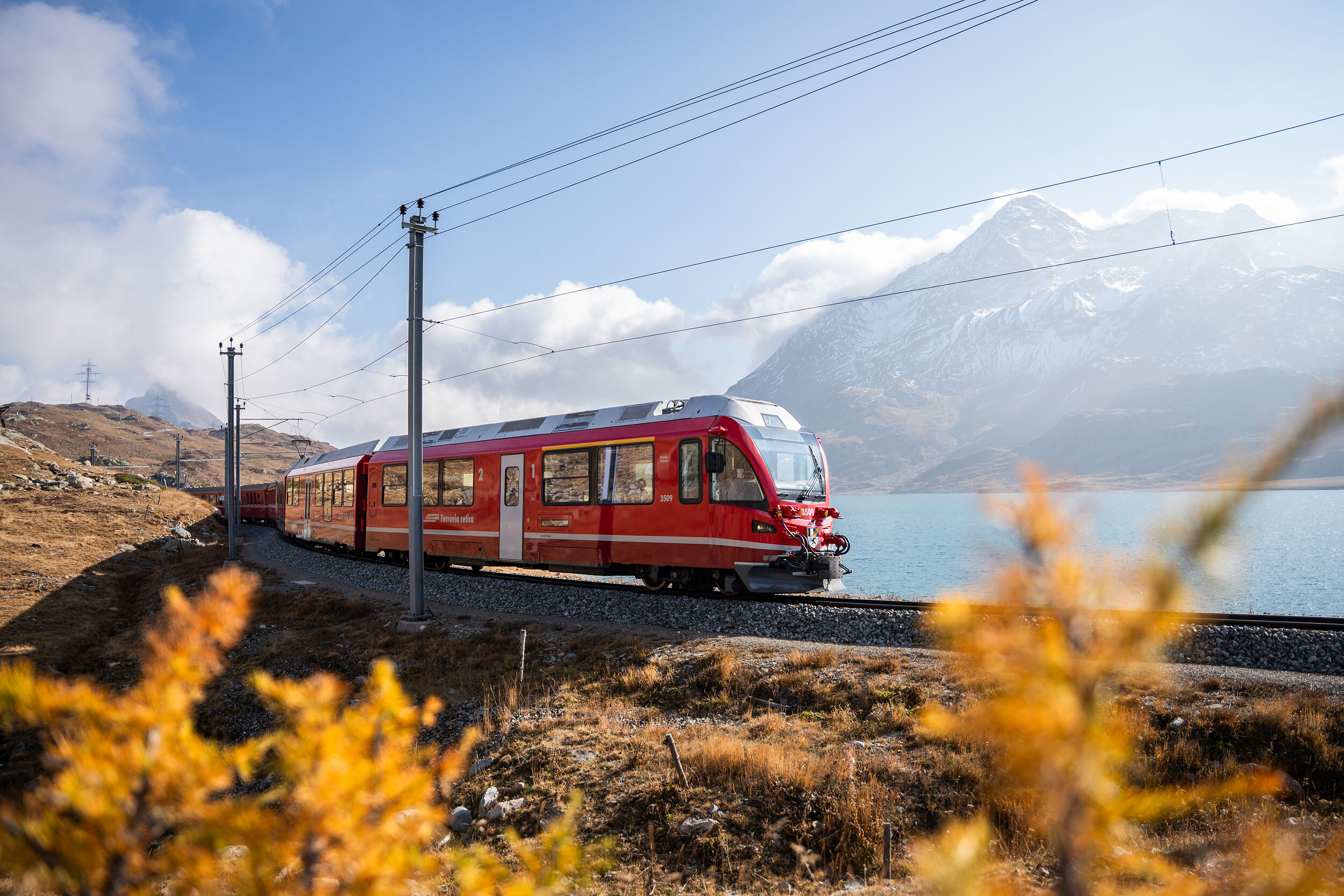 Ein Regionalzug der RhB fährt am herbstlichen Lago Bianco entlang.