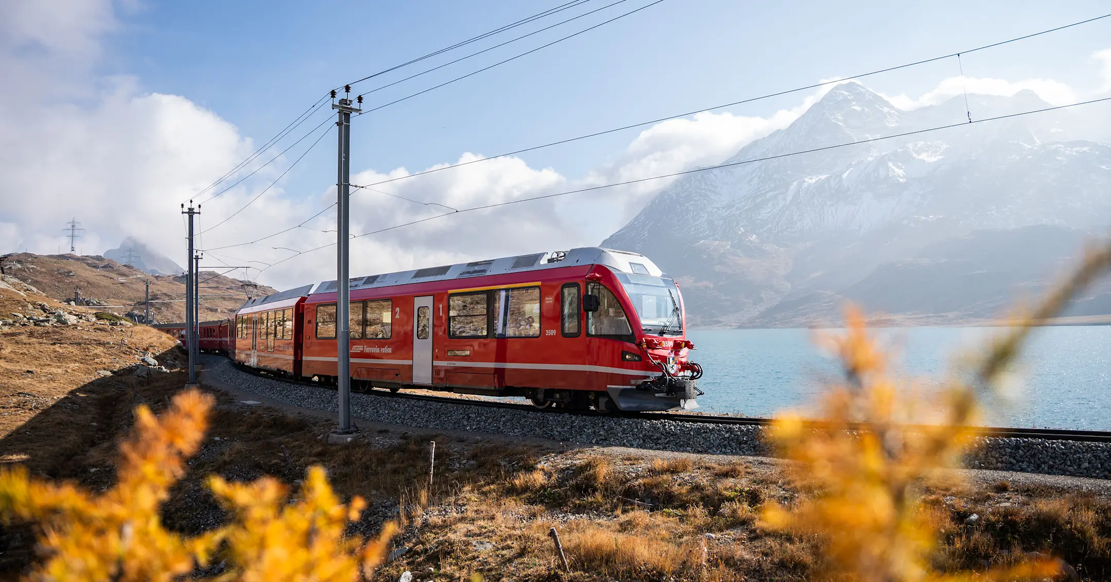 Ein Regionalzug der RhB fährt am herbstlichen Lago Bianco entlang.