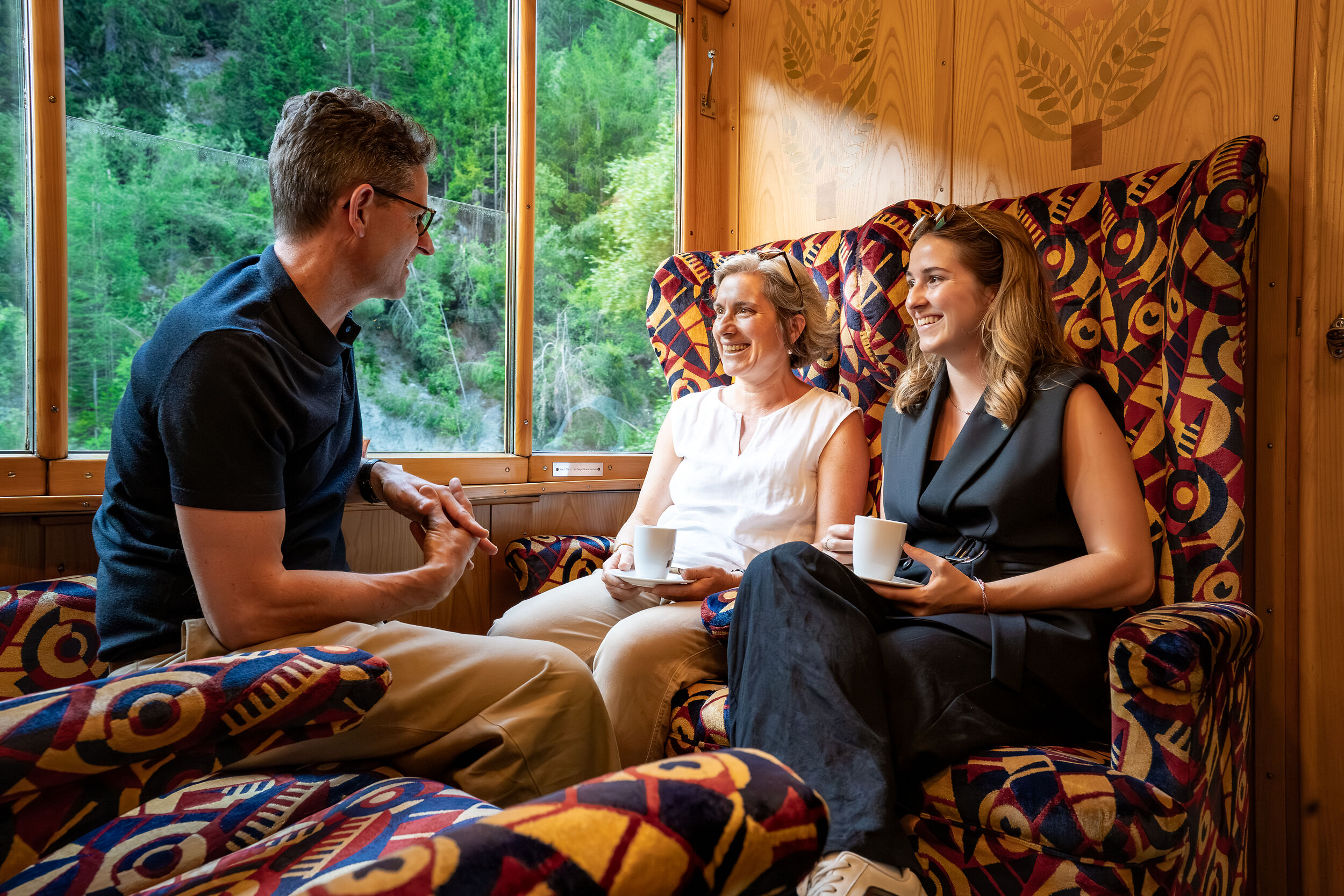 Drei Personen sitzen im Alpine Classic Pullman Salonwagen und unterhalten sich.