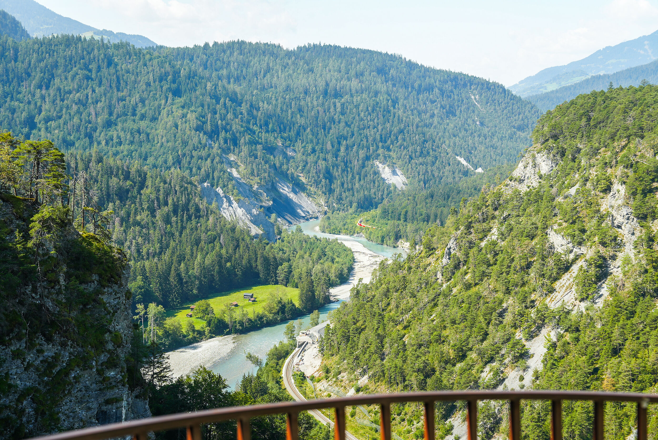 Ausblick von der Aussichtsplattform Zault in die Rheinschlucht. Im Hintergrund fährt ein RhB-Zug an der Felswand entlang. 