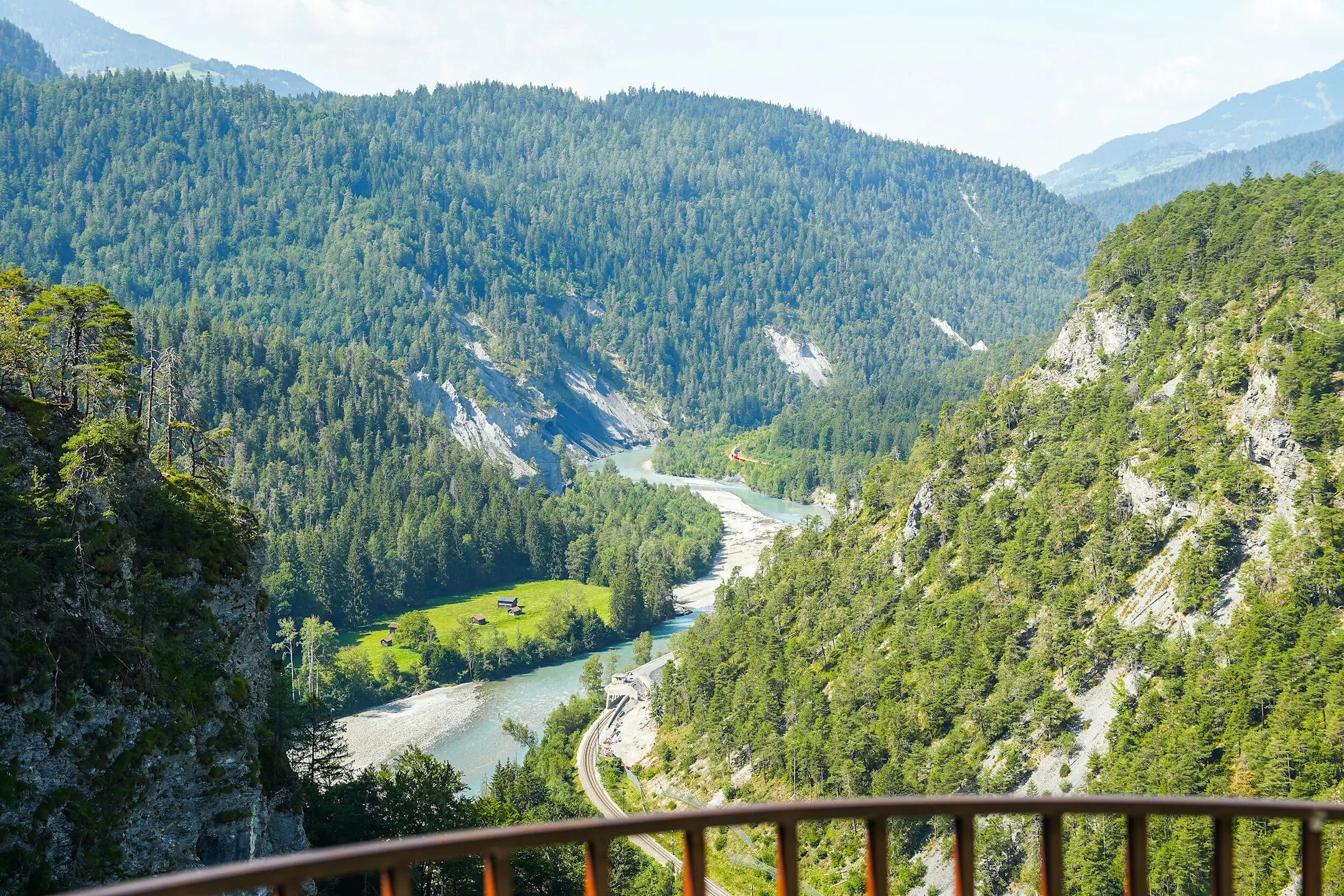 Ausblick von der Aussichtsplattform Zault in die Rheinschlucht. Im Hintergrund fährt ein RhB-Zug an der Felswand entlang.