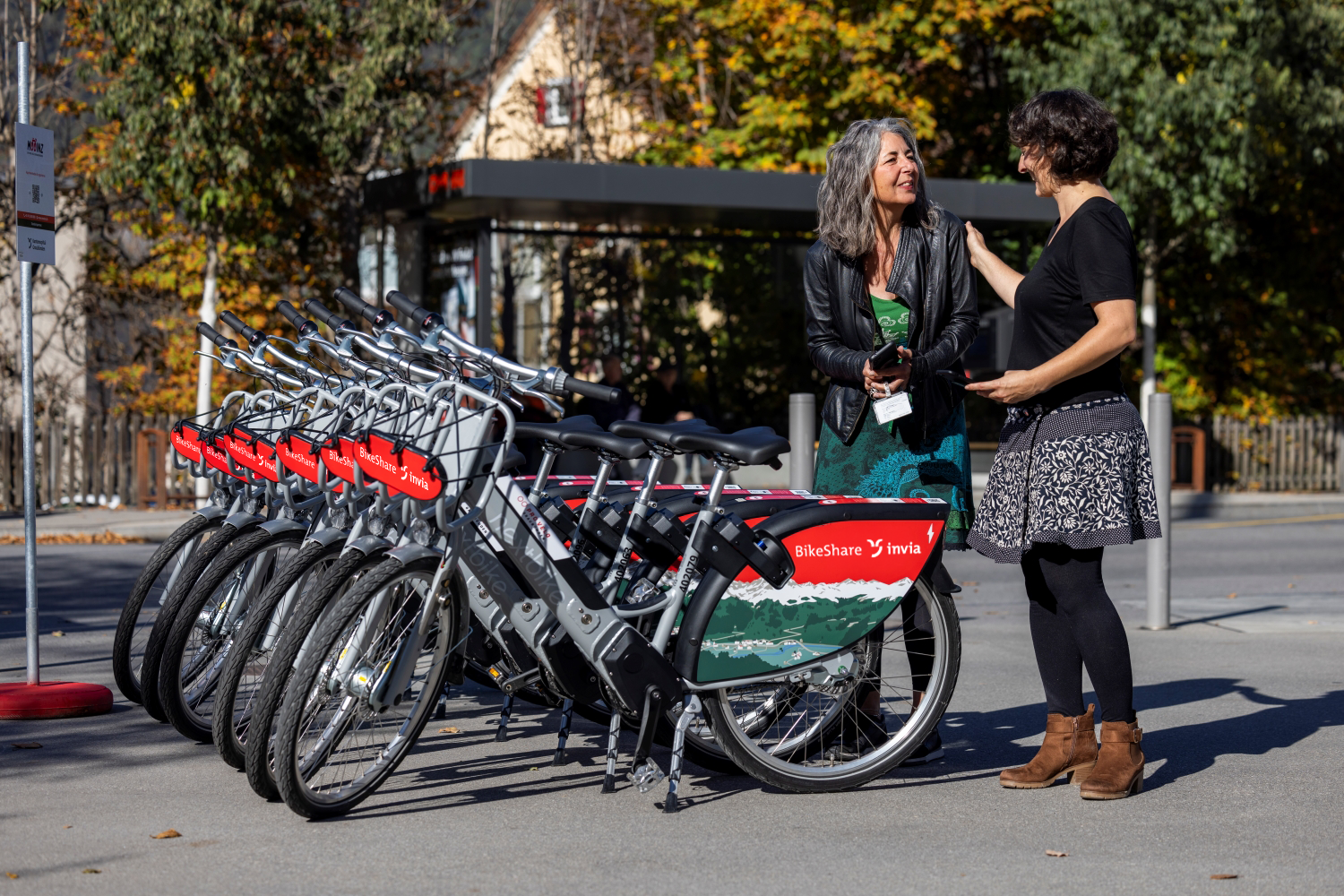 Zwei Frauen stehen vor Mooinz Bikesharing Velos und sprechen miteinander