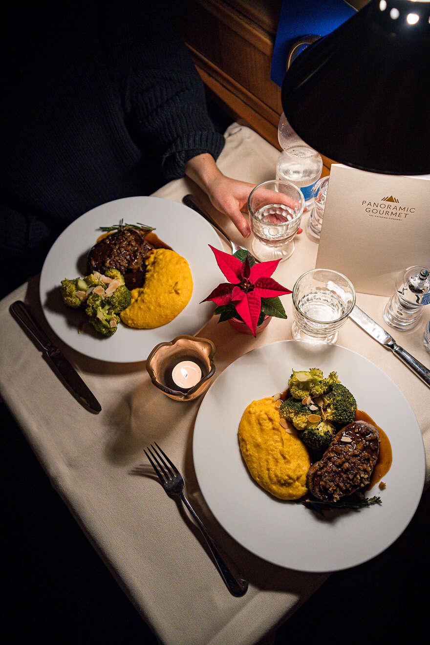 Due piatti elegantemente disposti con carne, polenta e verdure su un tavolo nella carrozza ristorante, a lume di candela.