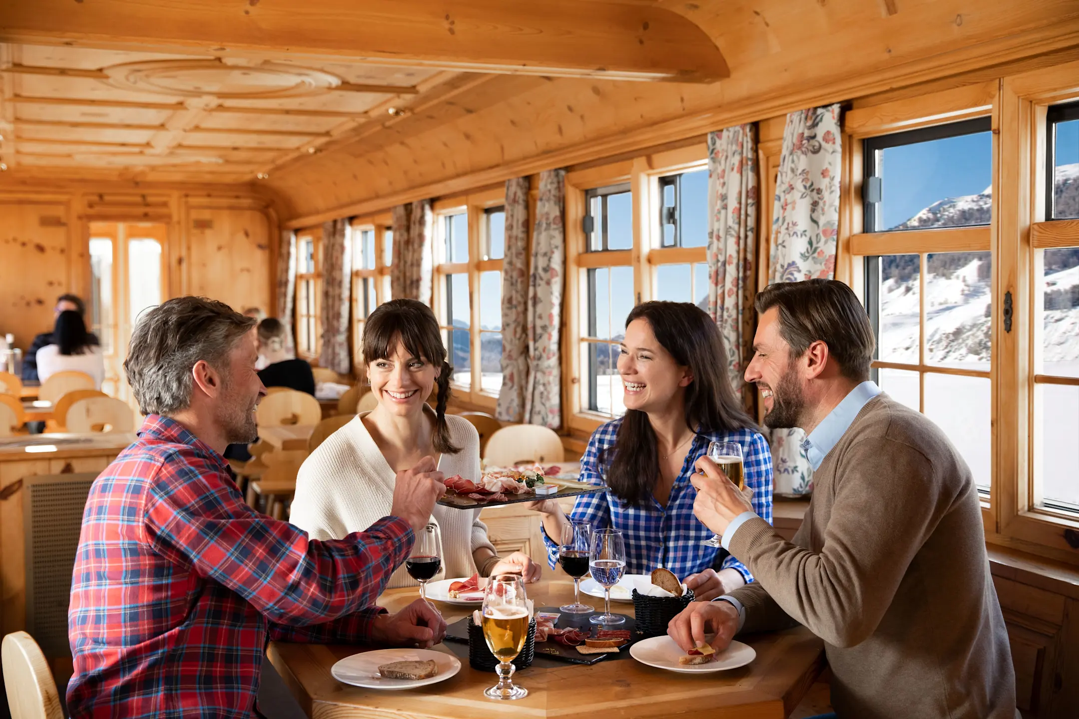 Vier Fahrgäste bedienen sich an einer Apéroplatte in der Stiva Retica.