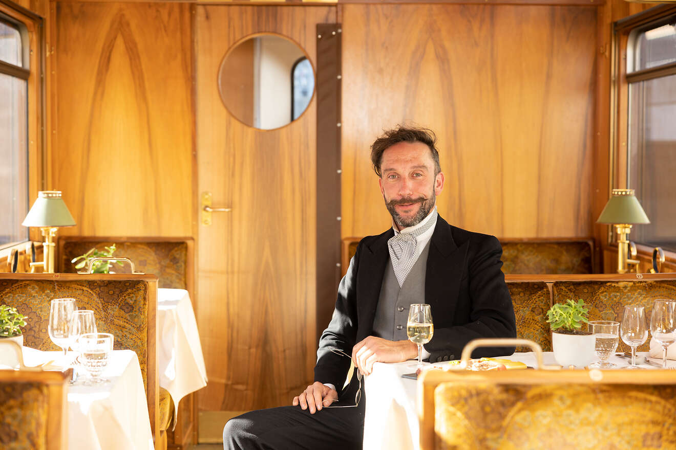Ein elegant gekleideter Mann mit Fliege sitzt in einem stilvollen Speisewagen des Welterbe Genussexpress.