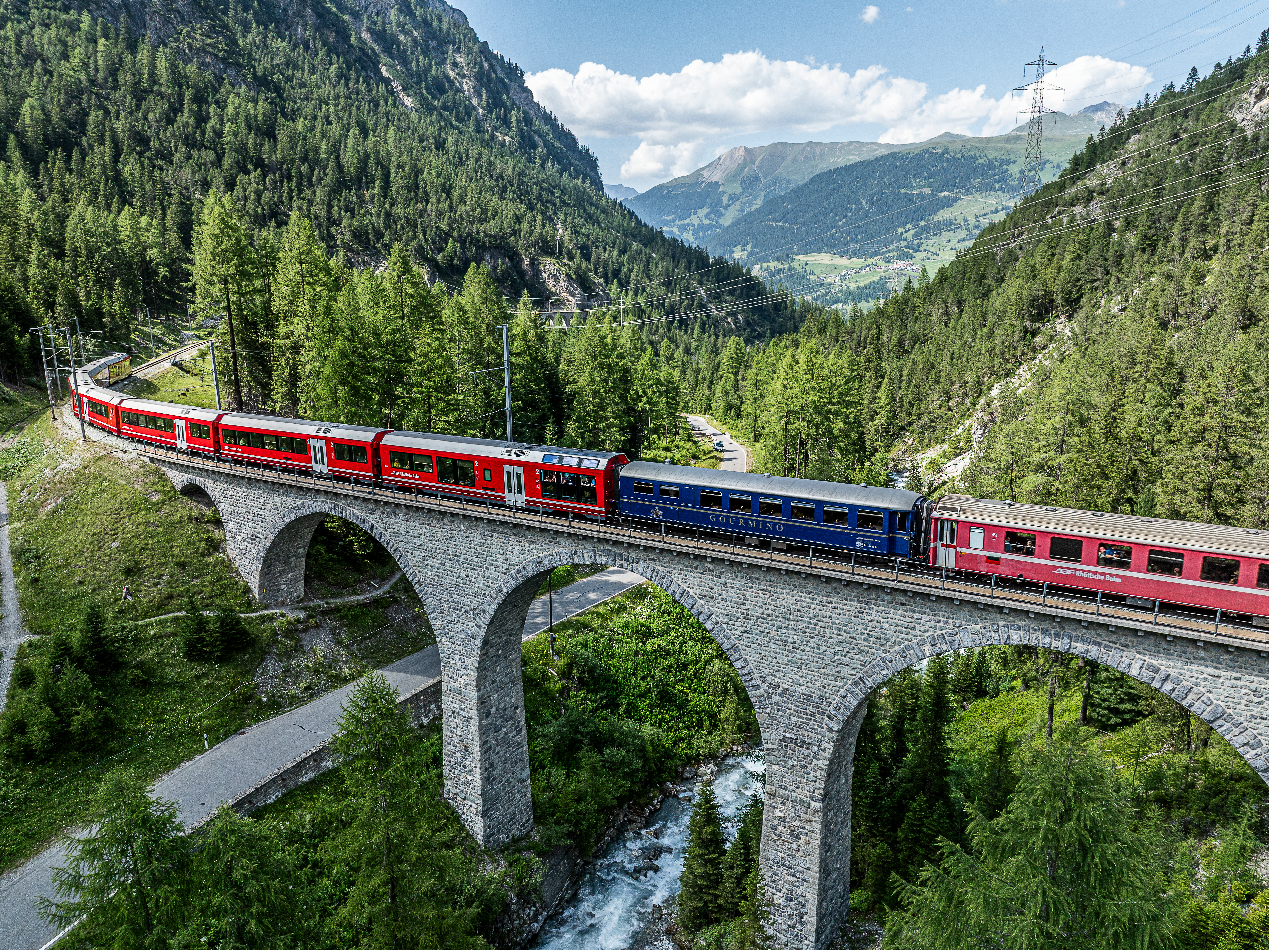 Der Speisewagen Gourmino der Rhätischen Bahn fährt im Sommer über ein Viadukt. Im Hintergrund Alpenpanorama