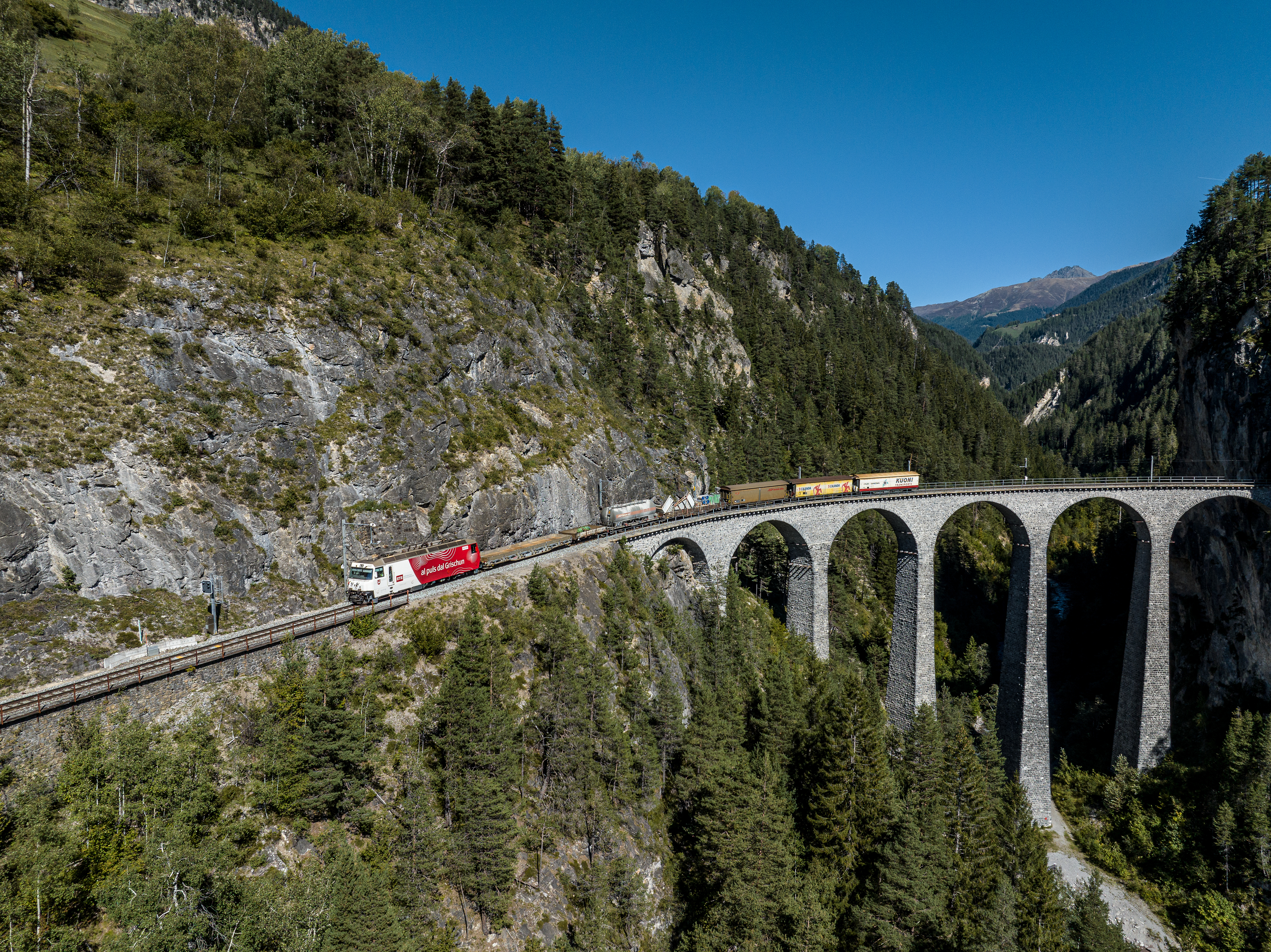 Ein Güterzug der RhB fährt im Sommer auf dem Landwasserviadukt mit unterschiedlichen Transportgütern