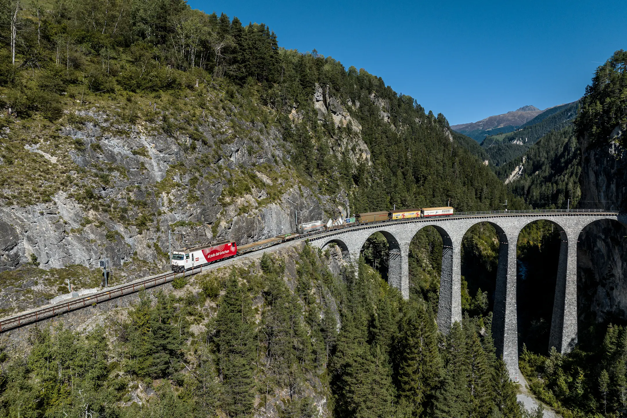 Ein Güterzug der RhB fährt im Sommer auf dem Landwasserviadukt mit unterschiedlichen Transportgütern
