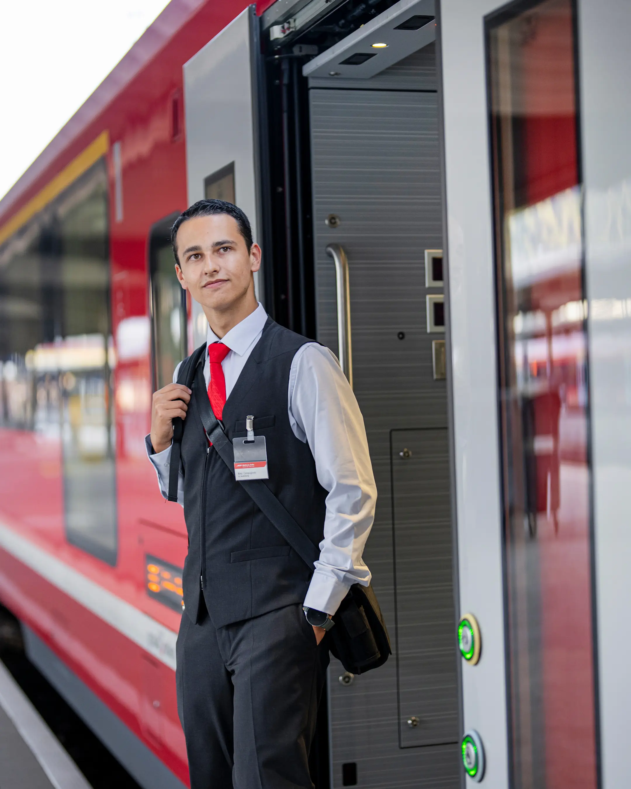 Ein Zugbegleiter steht vor der offenen Tür eines roten Zuges der Rhätischen Bahn
