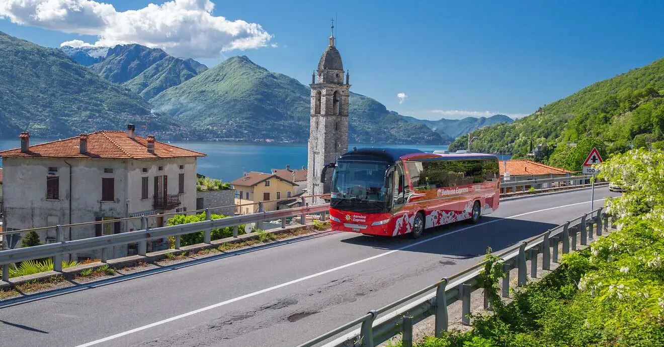 Bernina Express Bus in sunny weather on Lake Como. Picturesque village with church, lake and mountains in the background.