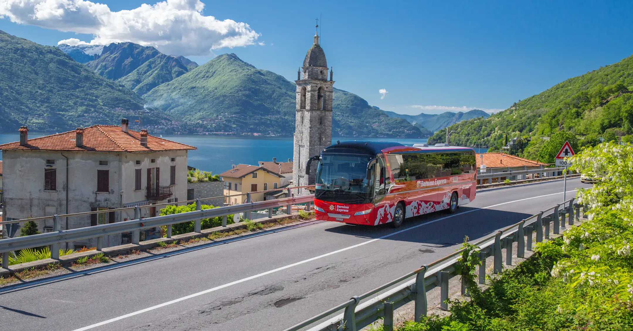 Bernina Express Bus in sunny weather on Lake Como. Picturesque village with church, lake and mountains in the background.