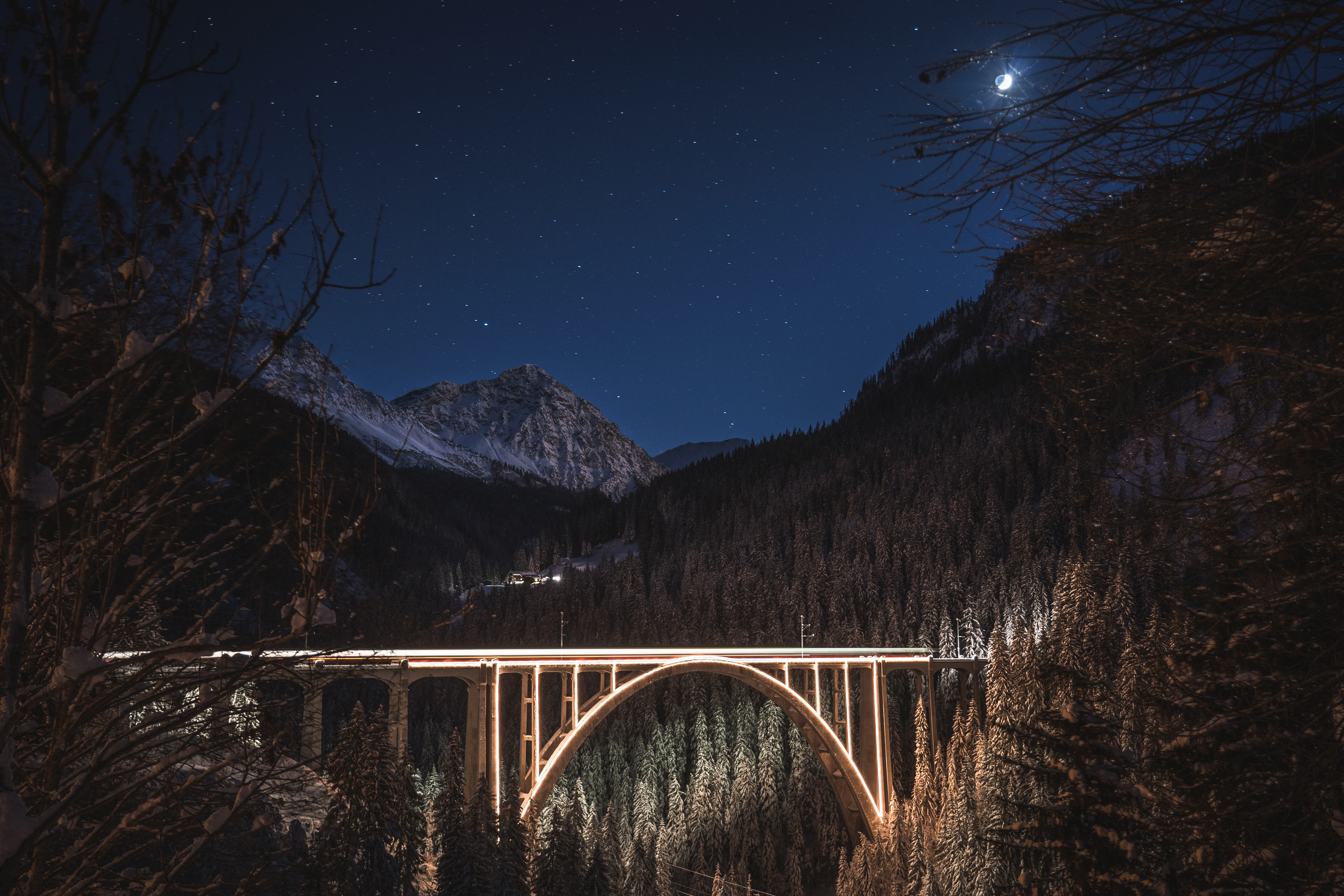 Beleuchteter Zug überquert bei Nacht den Langwieserviadukt inmitten einer winterlichen Berg- und Waldlandschaft.