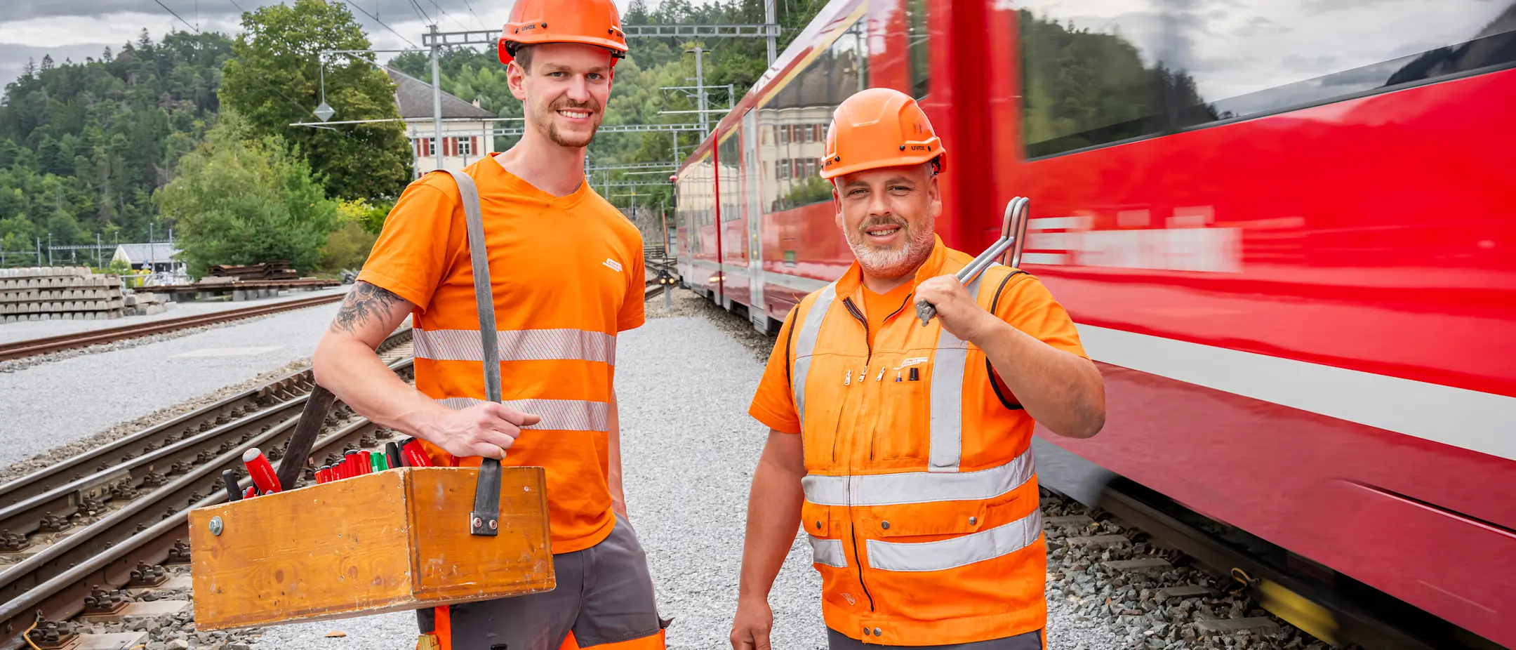Zwei Elektroinstallateure der RhB vor einem roten Zug der RhB am Bahnhof Reichenau-Tamins.