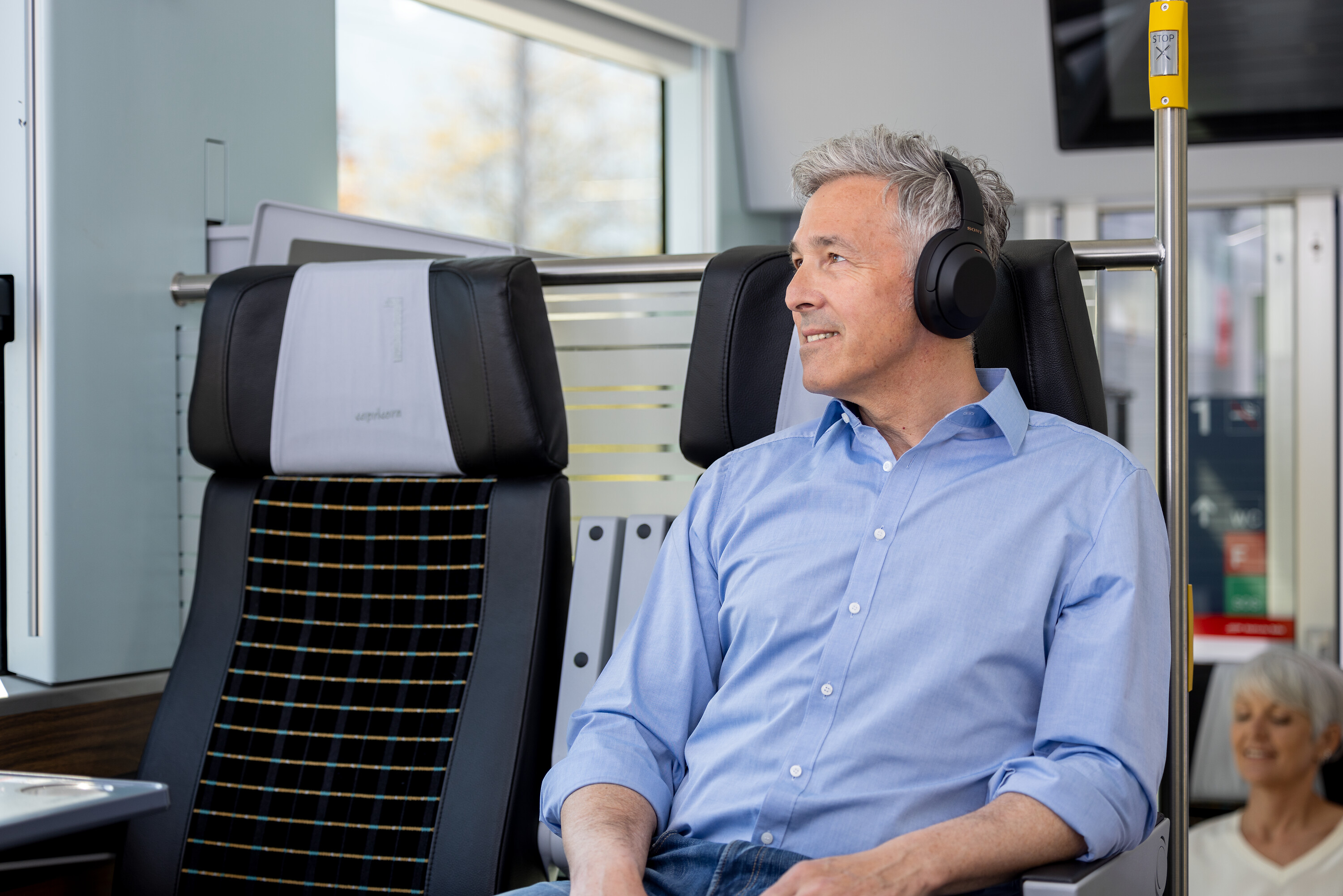 Reisender im Capricorn-Triebzug mit Hemd und kabellosen Kopfhörern im 1. Klasse-Abteil.