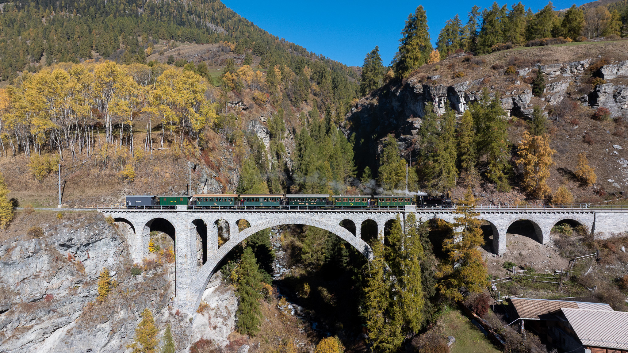 Die historische Dampflok Heidi überquert das Val Tuoi Viadukt vor herbstlicher Bergkulisse.