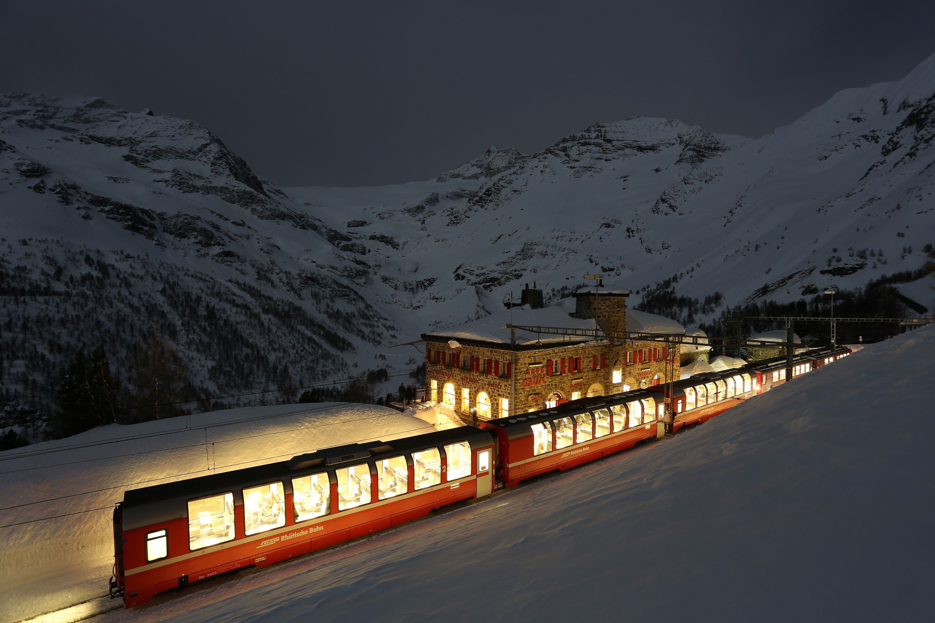 The illuminated Bernina Express on a full moon night at Alp Grüm station.