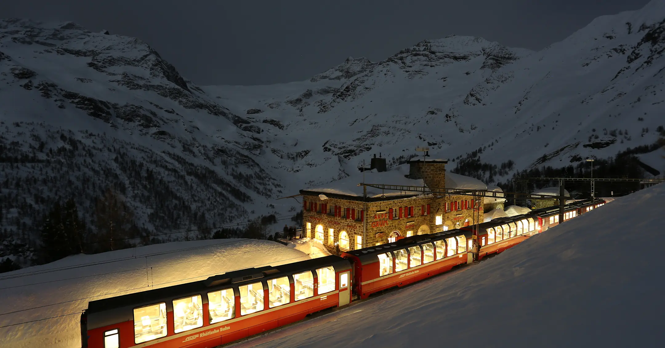Der beleuchtete Bernina Express in einer Vollmondnacht am Bahnhof Alp Grüm.