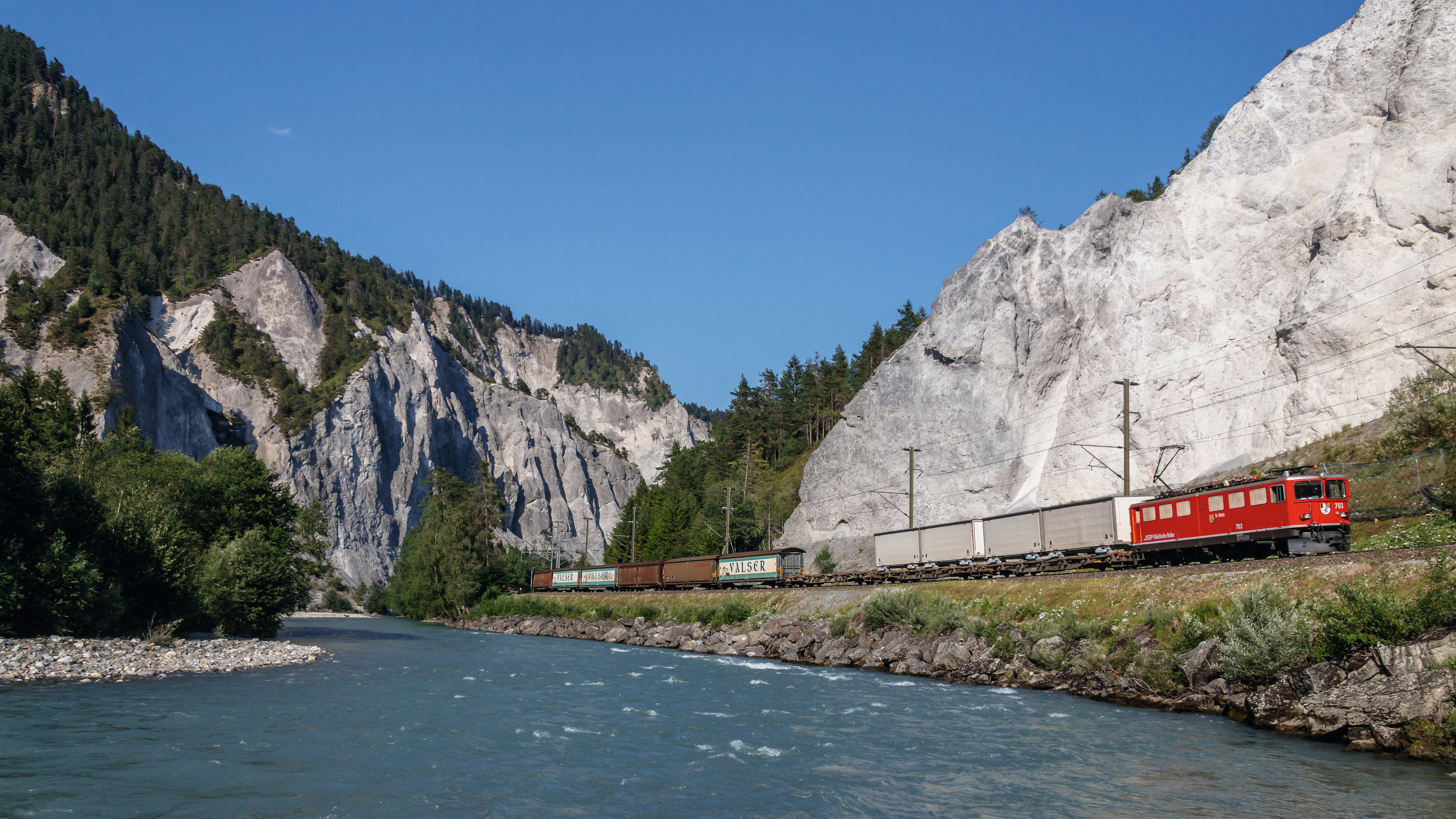 Ein Güterzug der Rhätischen Bahn mit unterschiedlichen Güterwagen fährt im Sommer durch die Rheinschlucht