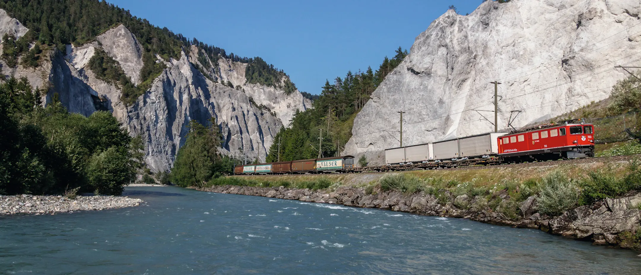 Ein Güterzug der Rhätischen Bahn mit unterschiedlichen Güterwagen fährt im Sommer durch die Rheinschlucht