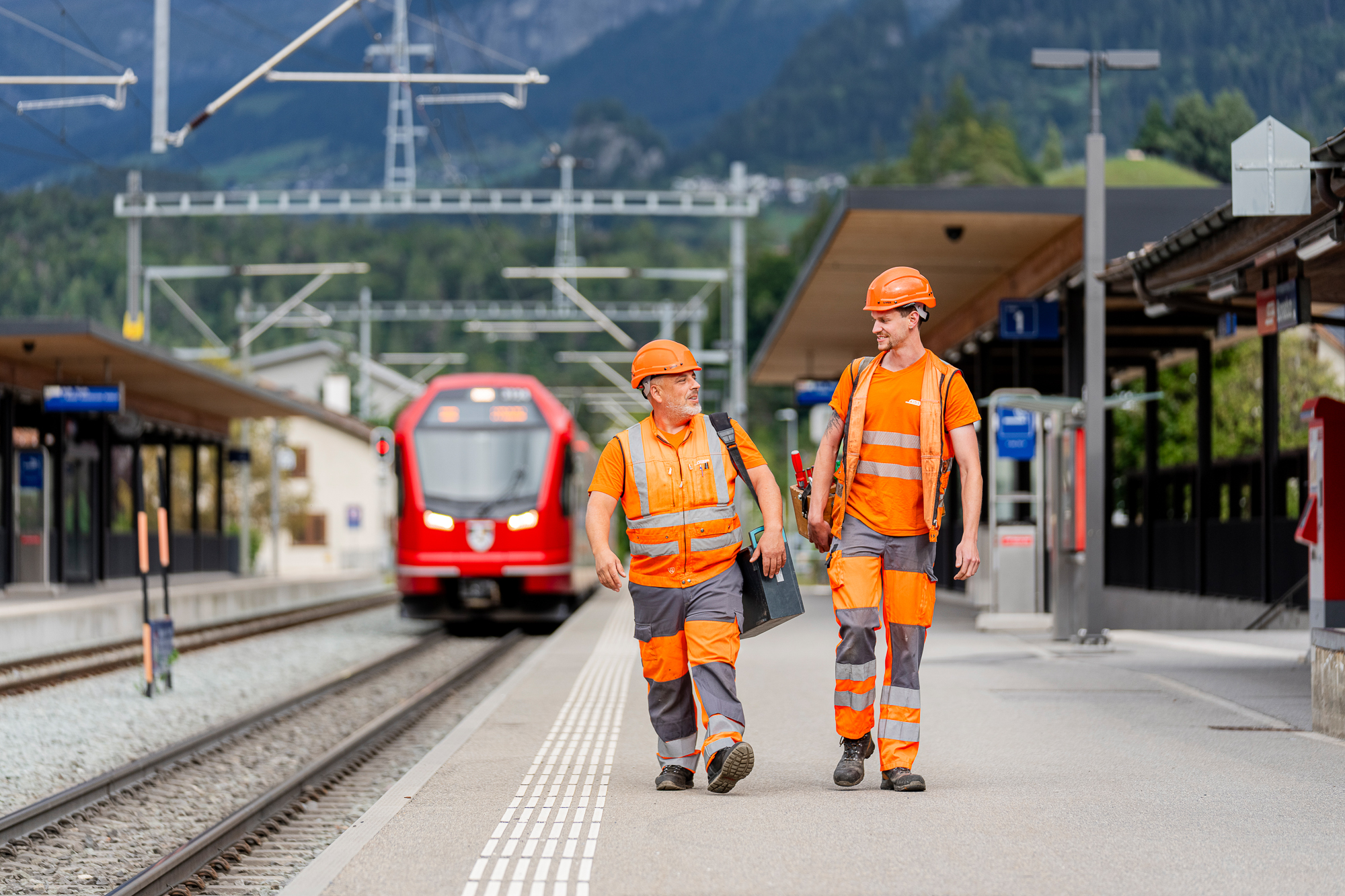 Zwei Mitarbeitende laufen am Bahnhof Bonaduz dem Gleis entlang