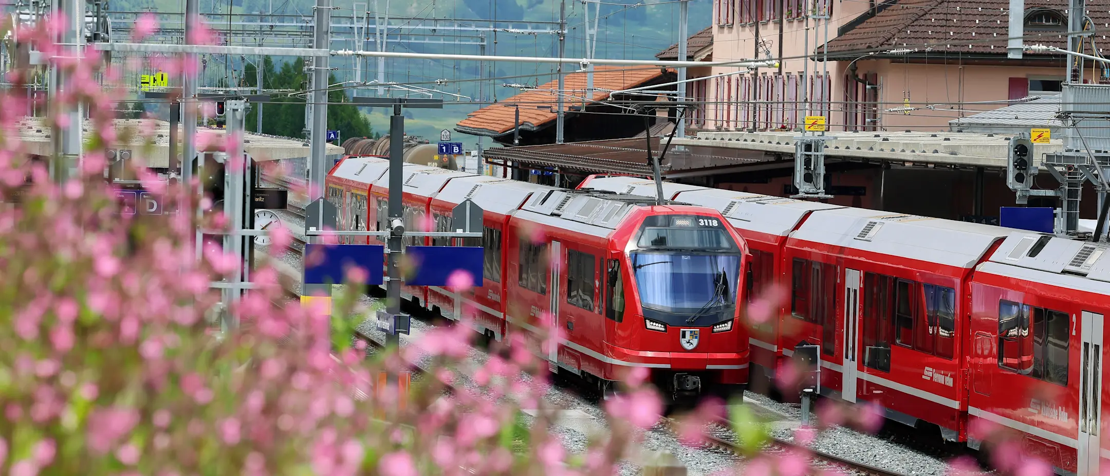 Ein Zug der Rhätischen Bahn bei der Bahnhofseröffnung in Pontresina mit Blumen im Vordergrund
