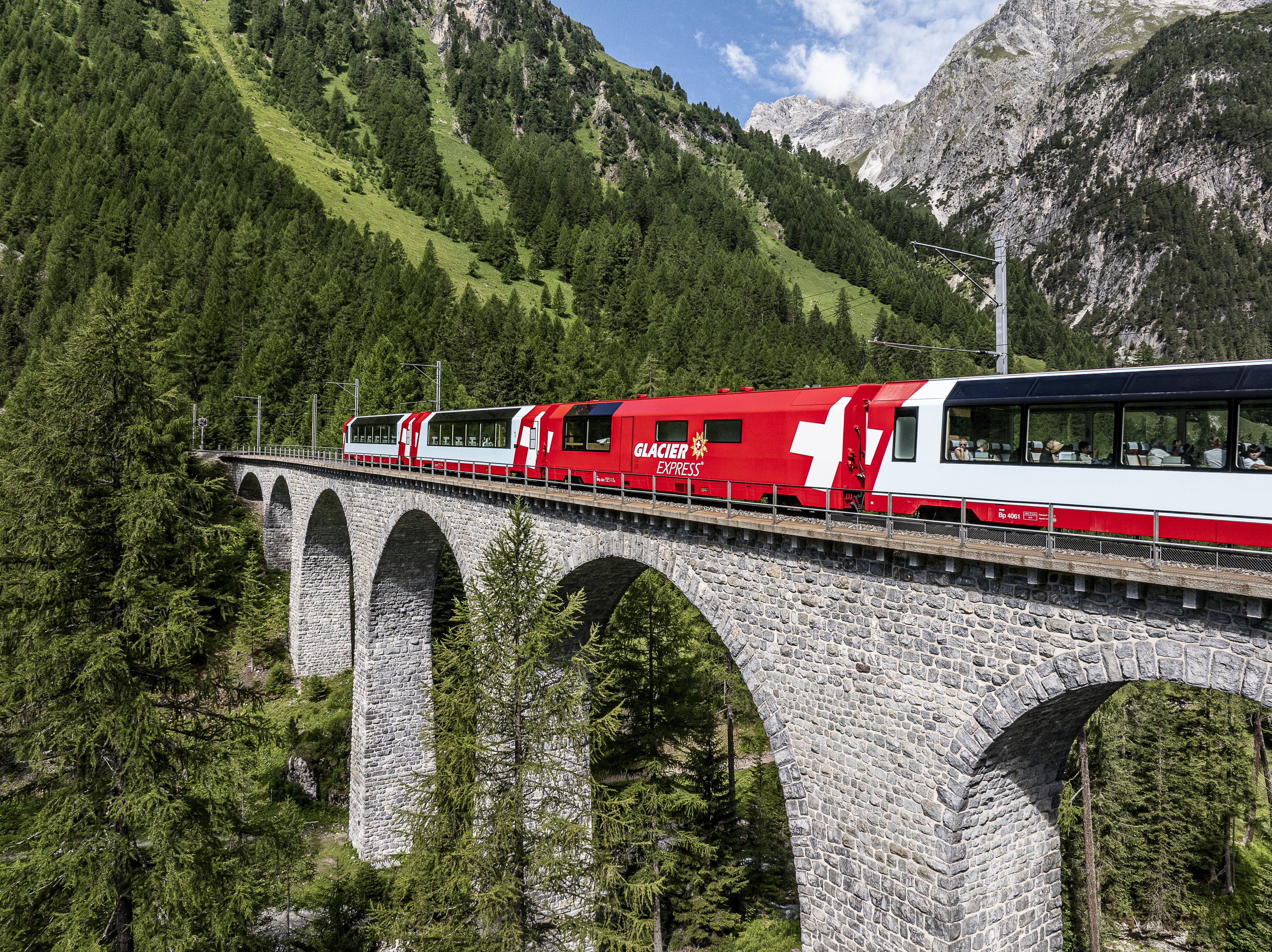 Der Glacier Express überquert ein steinernes Viadukt im Albulatal, umgeben von dichten Wäldern und alpiner Berglandschaft.