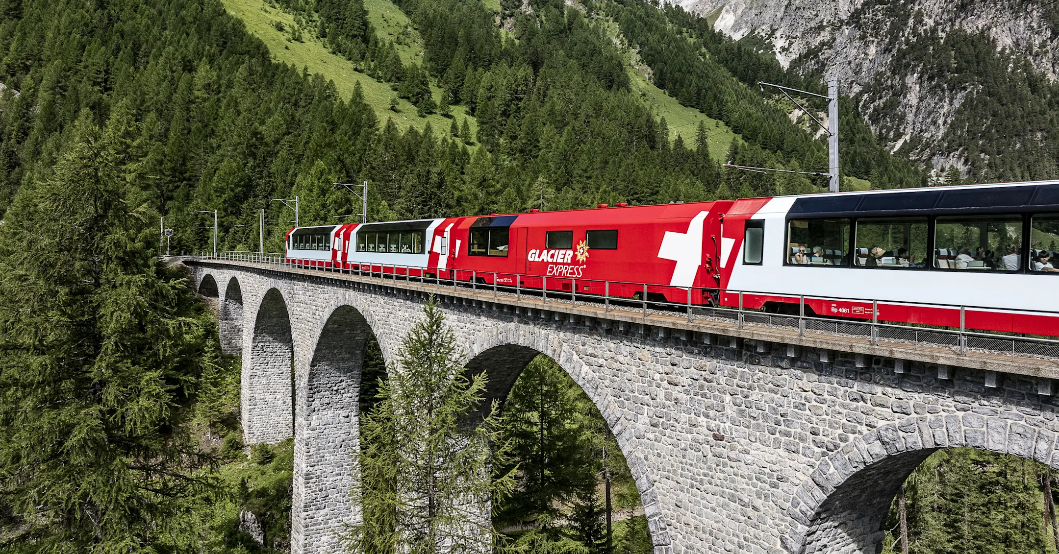 Der Glacier Express überquert ein steinernes Viadukt im Albulatal, umgeben von dichten Wäldern und alpiner Berglandschaft.