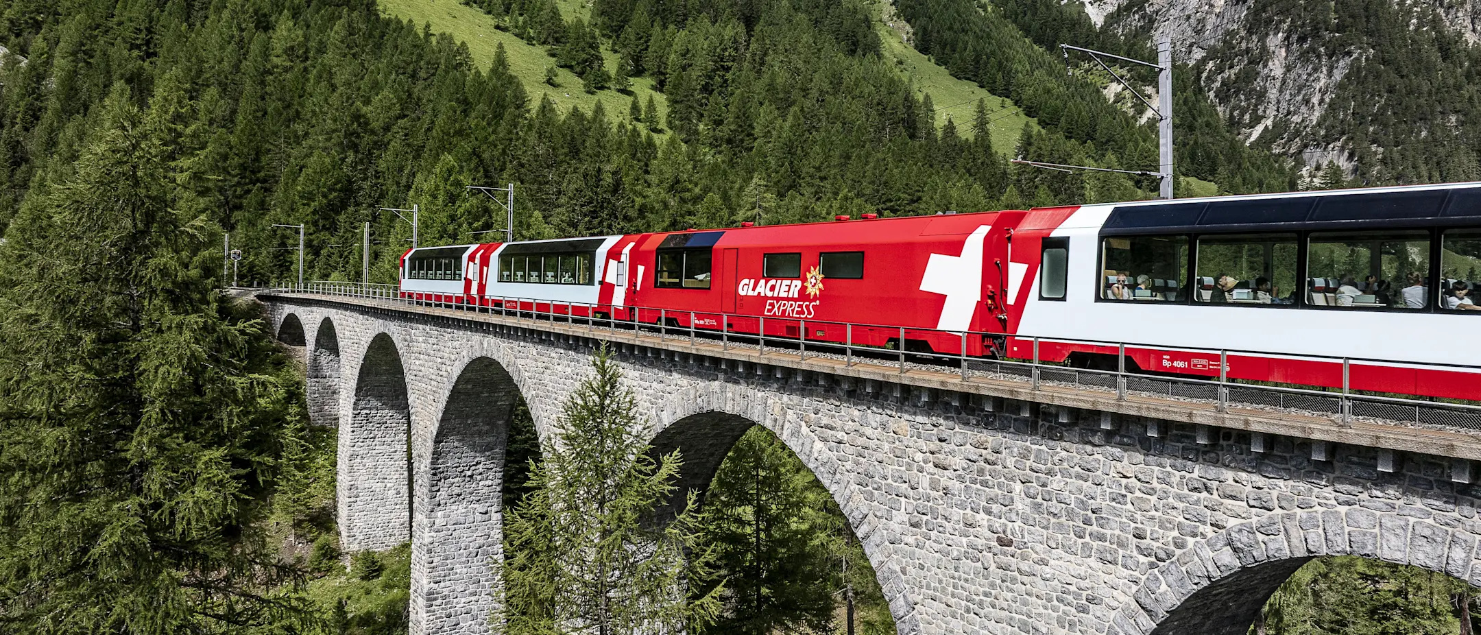Der Glacier Express überquert ein steinernes Viadukt im Albulatal, umgeben von dichten Wäldern und alpiner Berglandschaft.