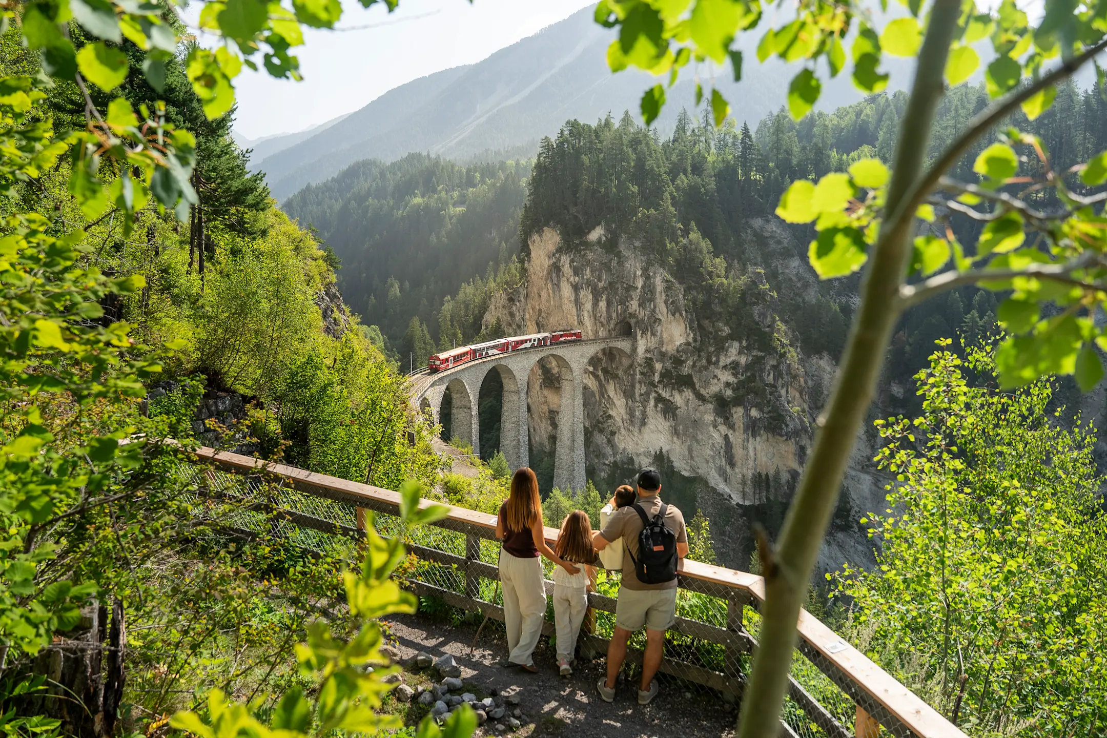 Una famiglia sulla piattaforma panoramica di Hennings. Sullo sfondo, un treno rosso che attraversa il viadotto di Landwasser.