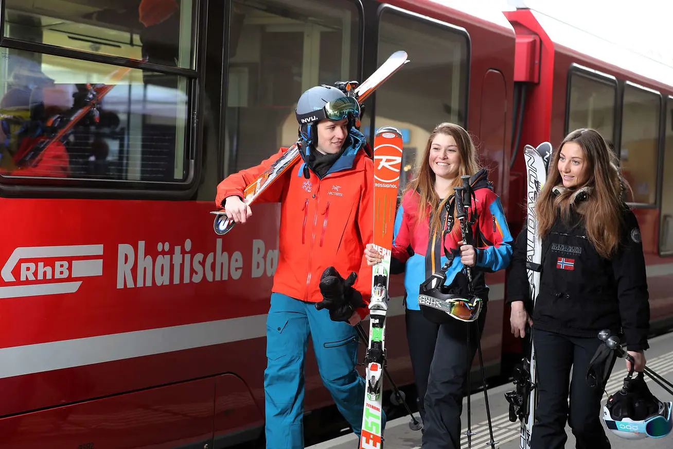 Drei Skifahrer laufen vor einem RhB Zug
